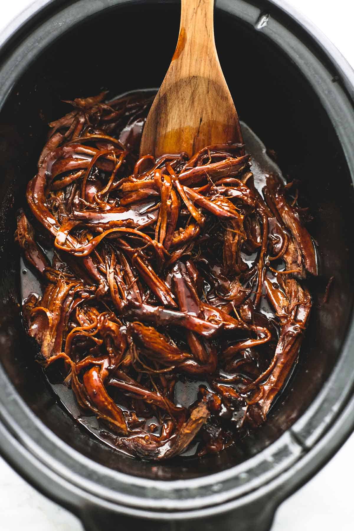 top view of slow cooker honey bbq beef brisket with a wooden serving spoon in a slow cooker.