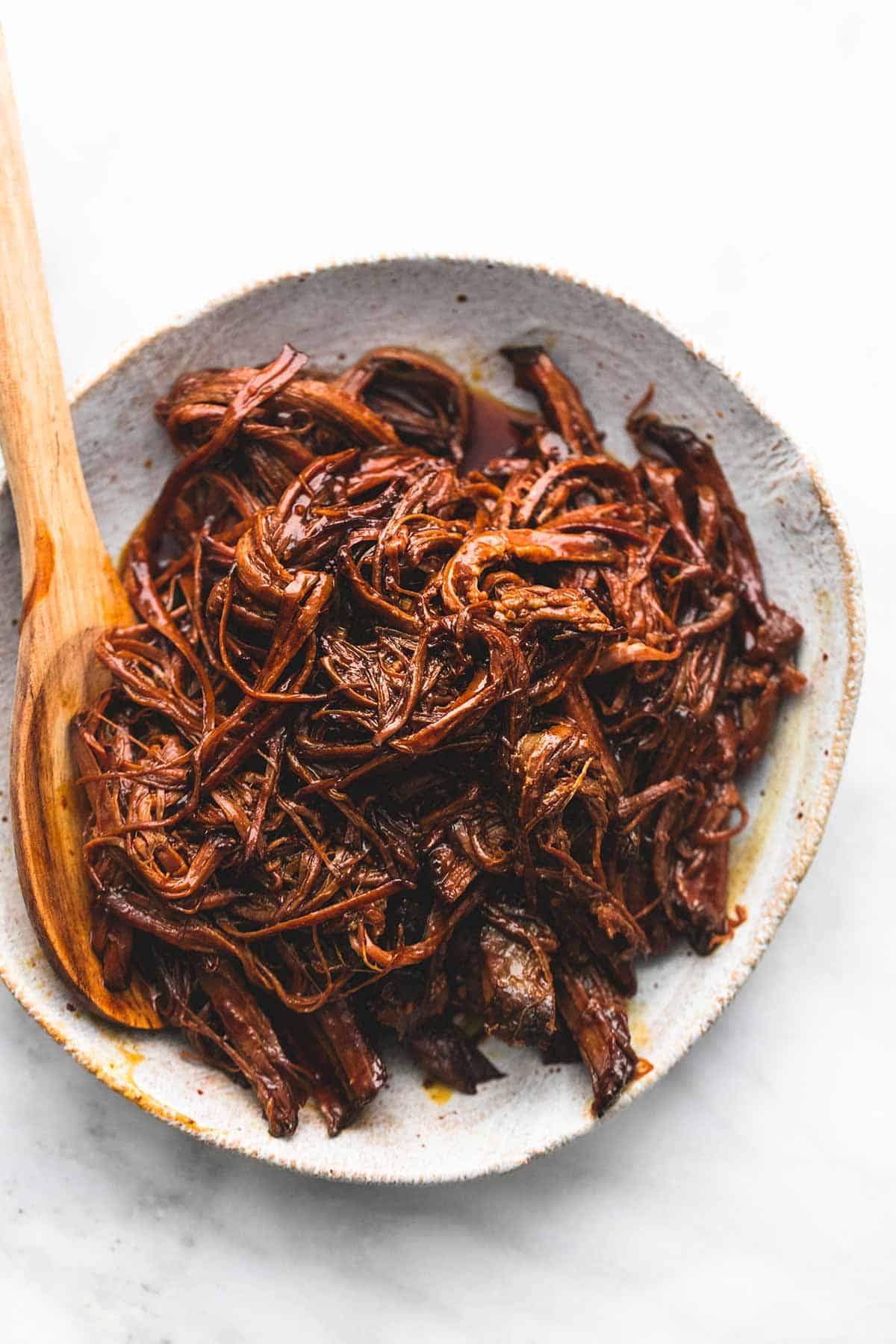 top view of slow cooker honey bbq beef brisket with a wooden serving spoon on a plate.