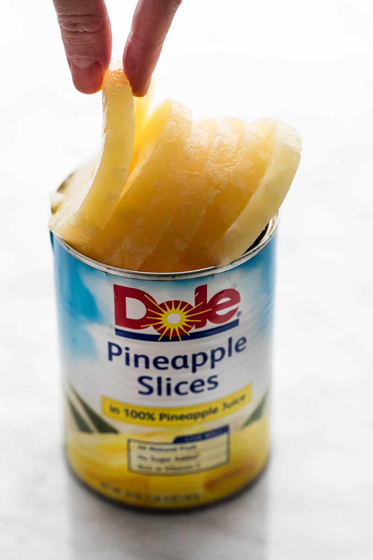 a hand grabbing a pineapple slice from a can of Dole pineapple slices.