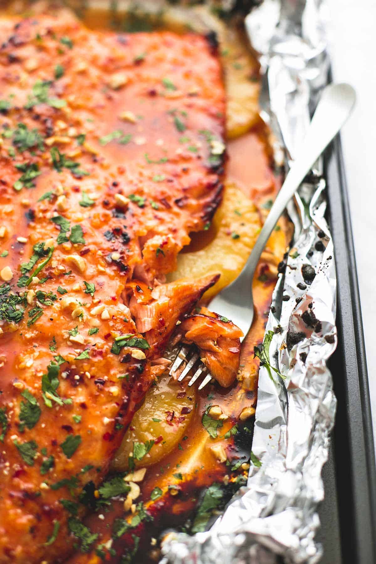 close up of baked Thai pineapple salmon in foil with a bite on a fork all on a baking sheet.