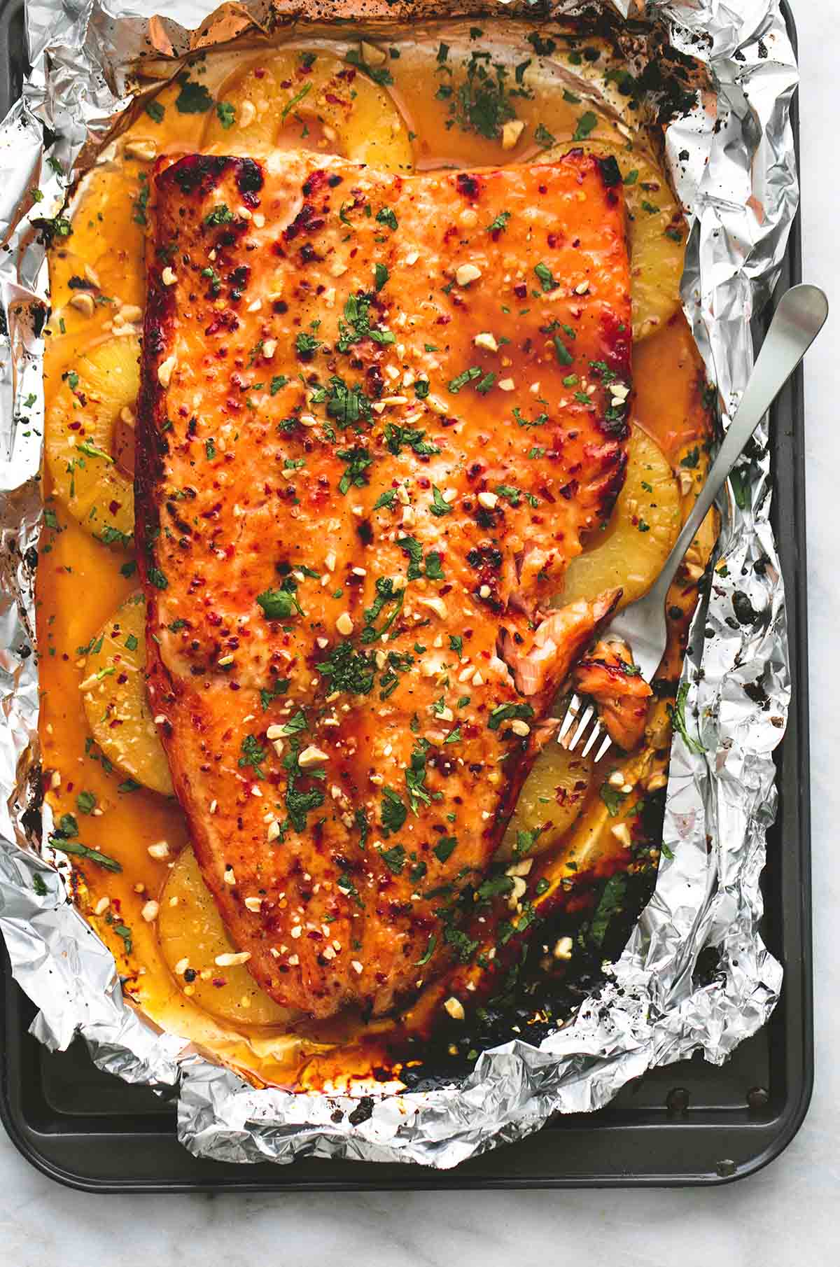 top view of baked Thai pineapple salmon in foil with a bite on a fork all on a baking sheet.