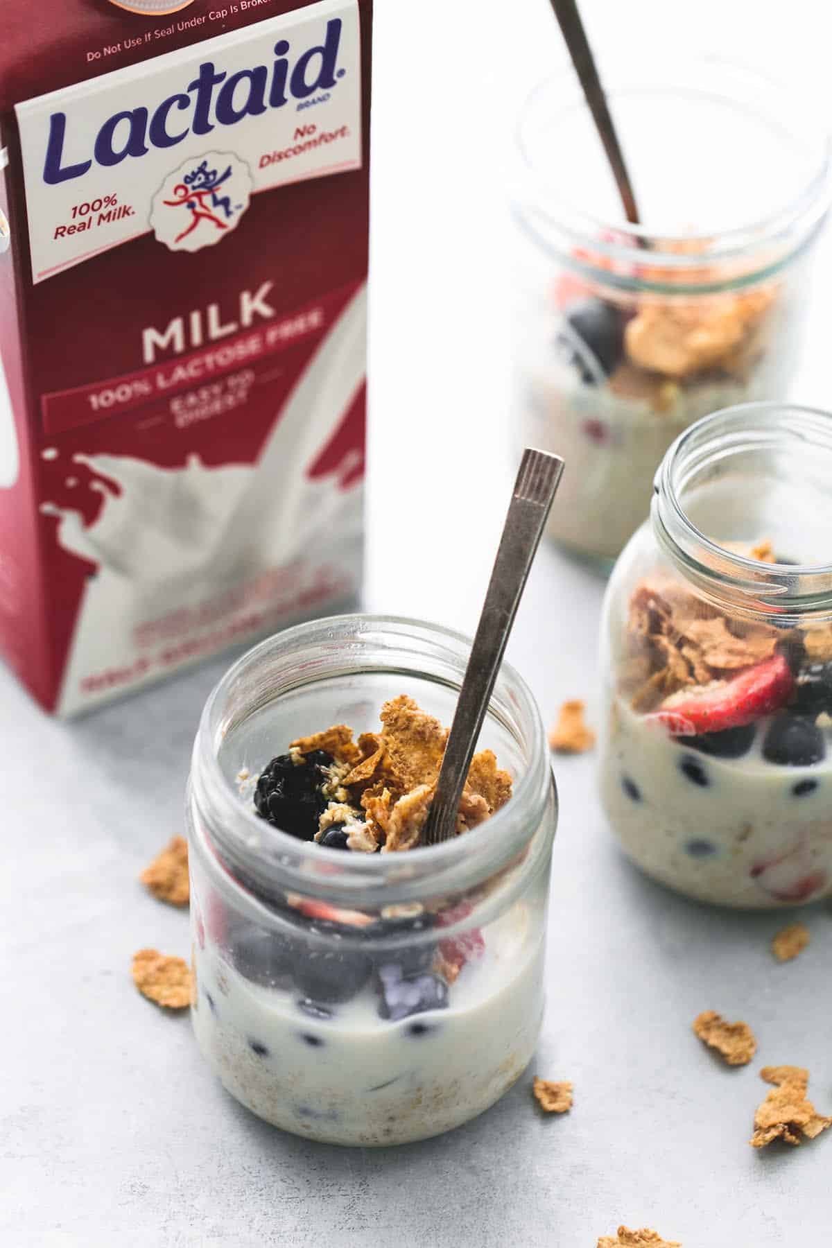 berry crunch overnight oats with spoons in jars with a container of Lactaid milk on the side.