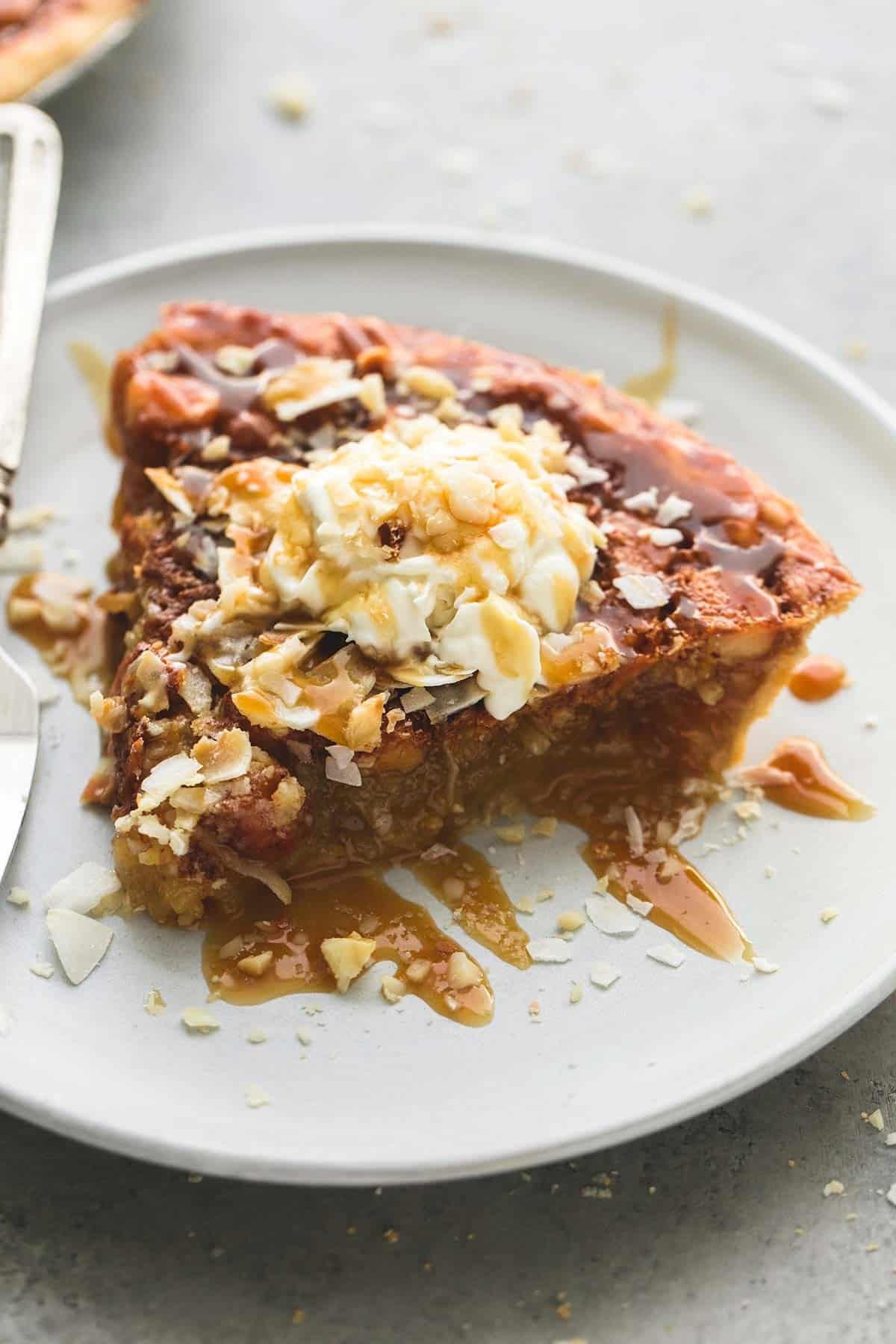 Caramel Coconut Macadamia Nut Pie | lecremedelacrumb.com a slice of caramel coconut macadamia nut pie topped with whipped cream coconut shavings and caramel sauce on a plate.
