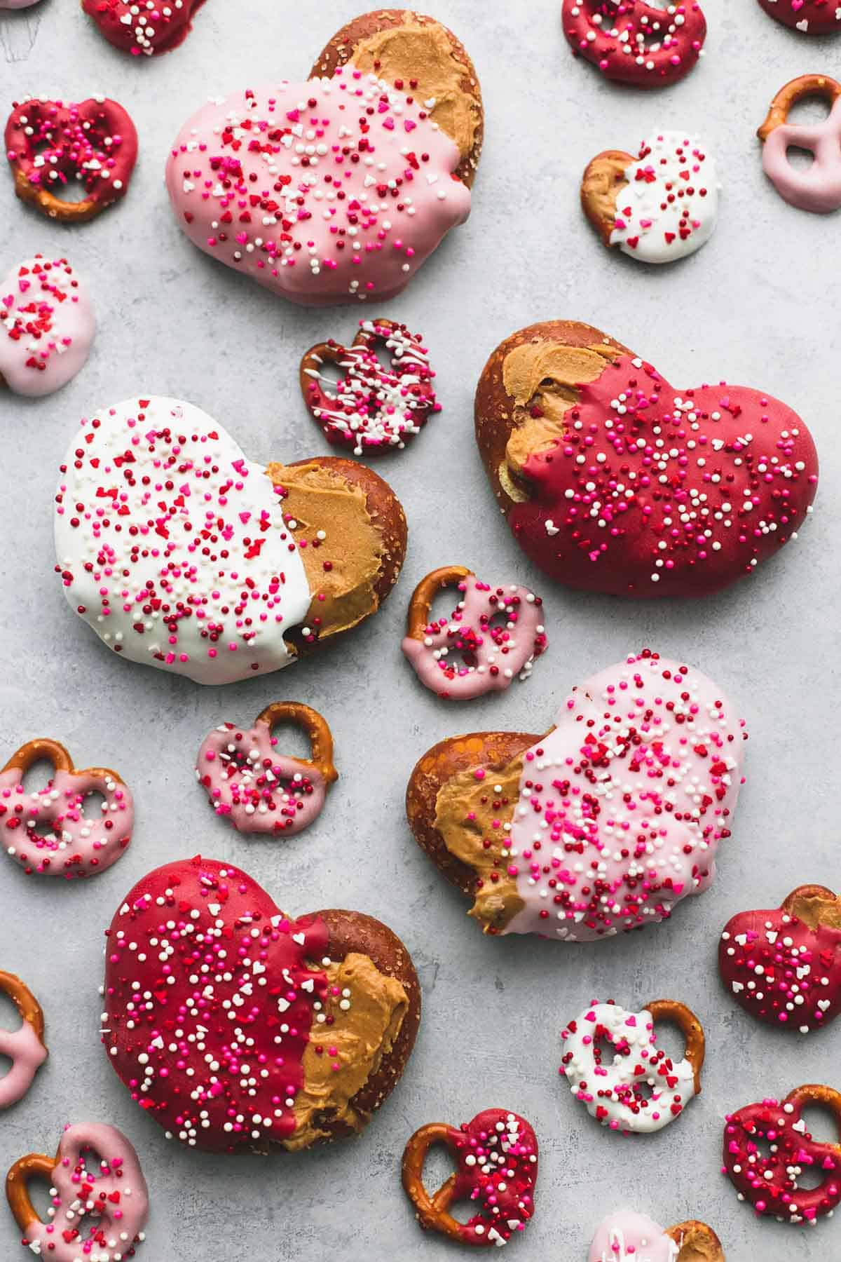 top view of big and small chocolate peanut butter pretzel hearts half covered in colored melting chocolate and sprinkles.