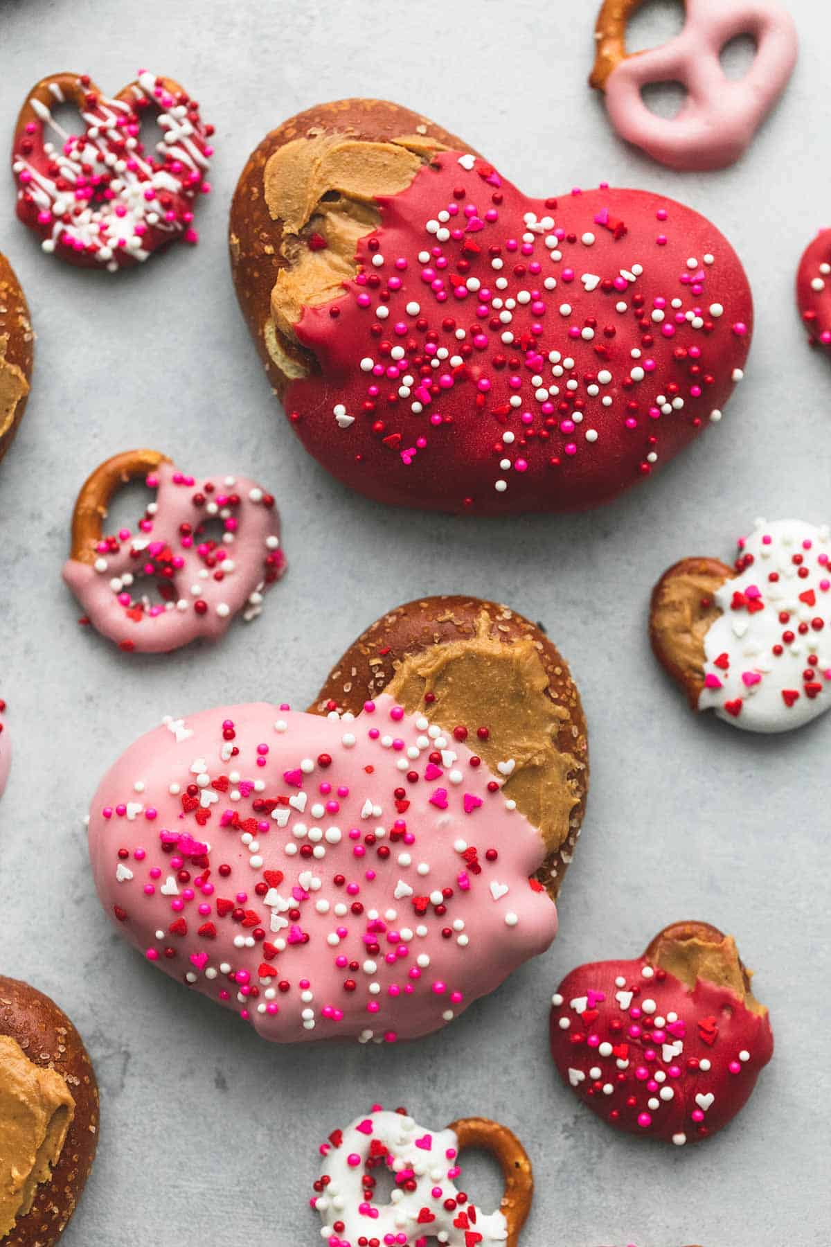 top view of big and small chocolate peanut butter pretzel hearts half covered in colored melting chocolate and sprinkles.