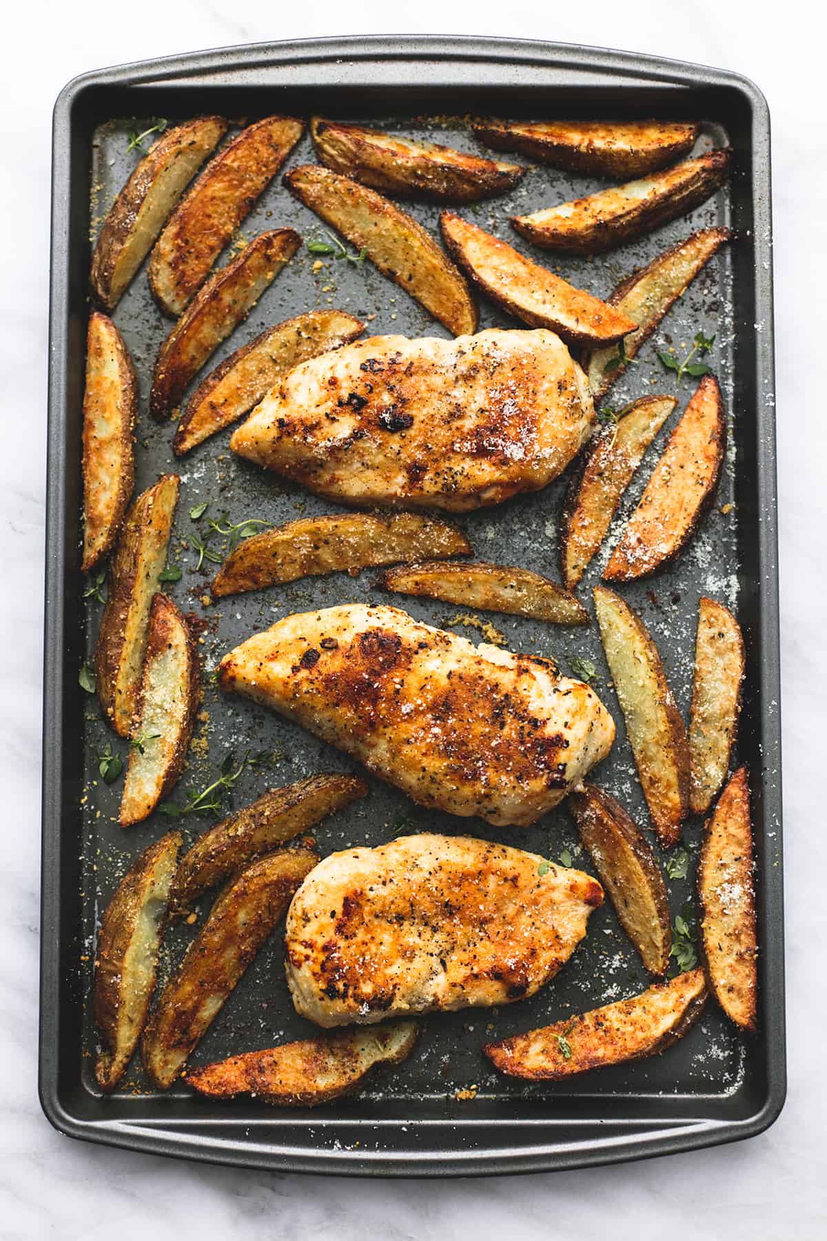 top view of garlic parmesan chicken & potatoes on a baking sheet.