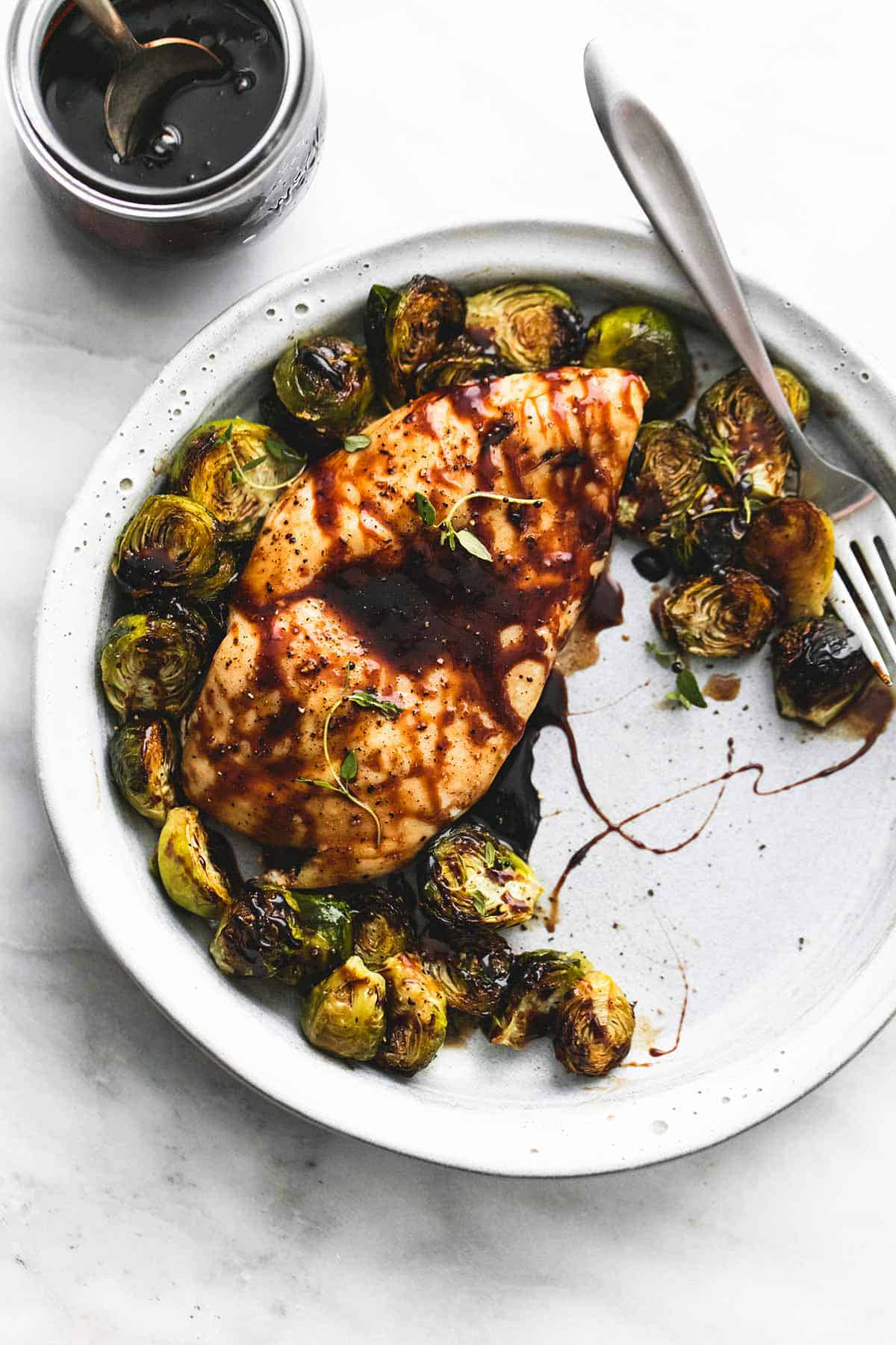 top view of honey balsamic chicken & brussels sprouts with a fork on a plate with a jar of sweet and tangy glaze with a spoon on the side.