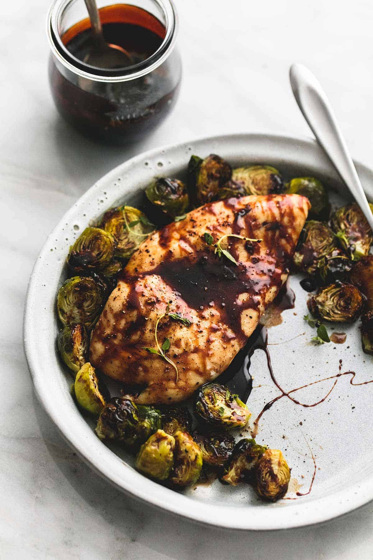 honey balsamic chicken & brussels sprouts with a fork on a plate with a jar of sweet and tangy glaze with a spoon on the side.