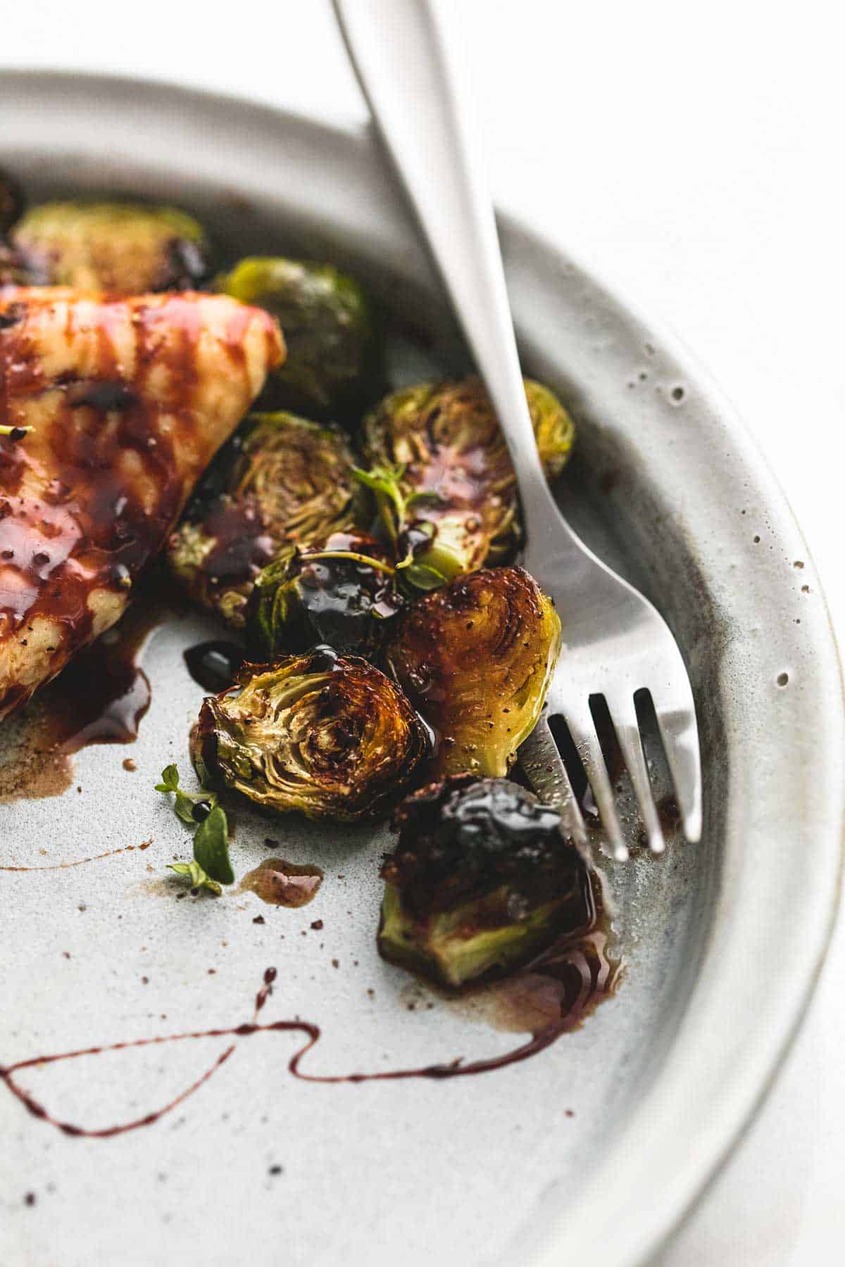 close up of honey balsamic chicken & brussels sprouts with a fork on a plate.