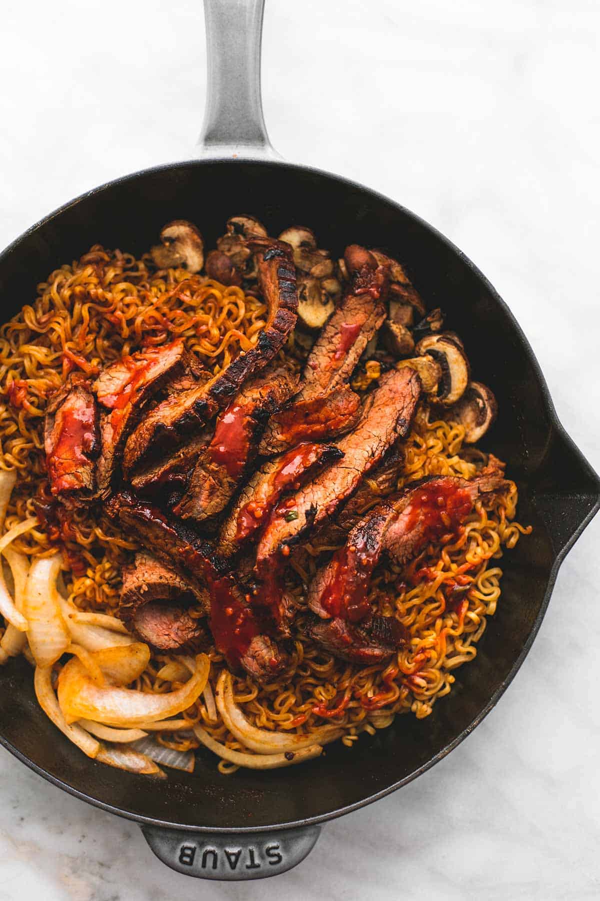 top view of spicy Korean beef noodles with meat, onions, and mushrooms on top in a skillet.