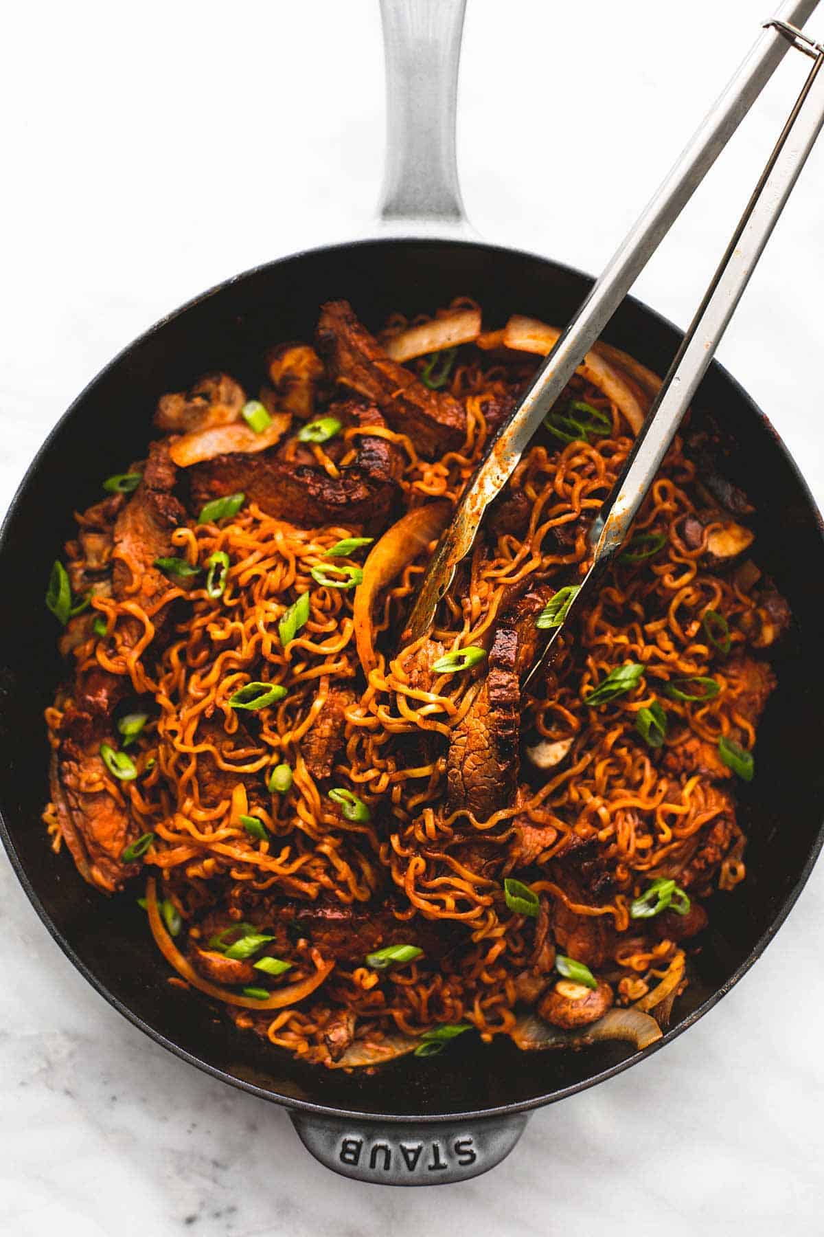 top view of spicy Korean beef noodles with tongs in a skillet.