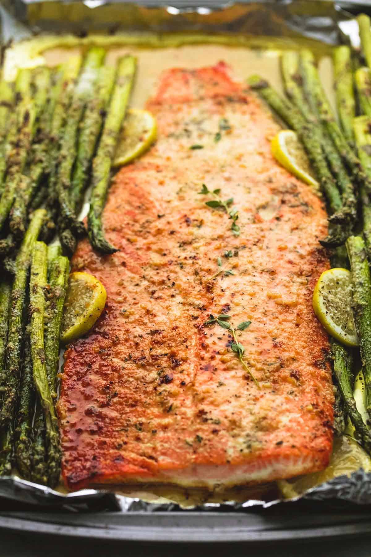 close up of baked lemon parmesan salmon & asparagus in foil in a baking sheet.