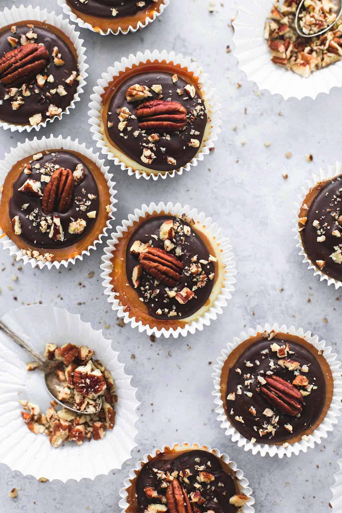 top view of mini turtle cheesecakes with more liners with crushed pecans and spoons in them on the side.