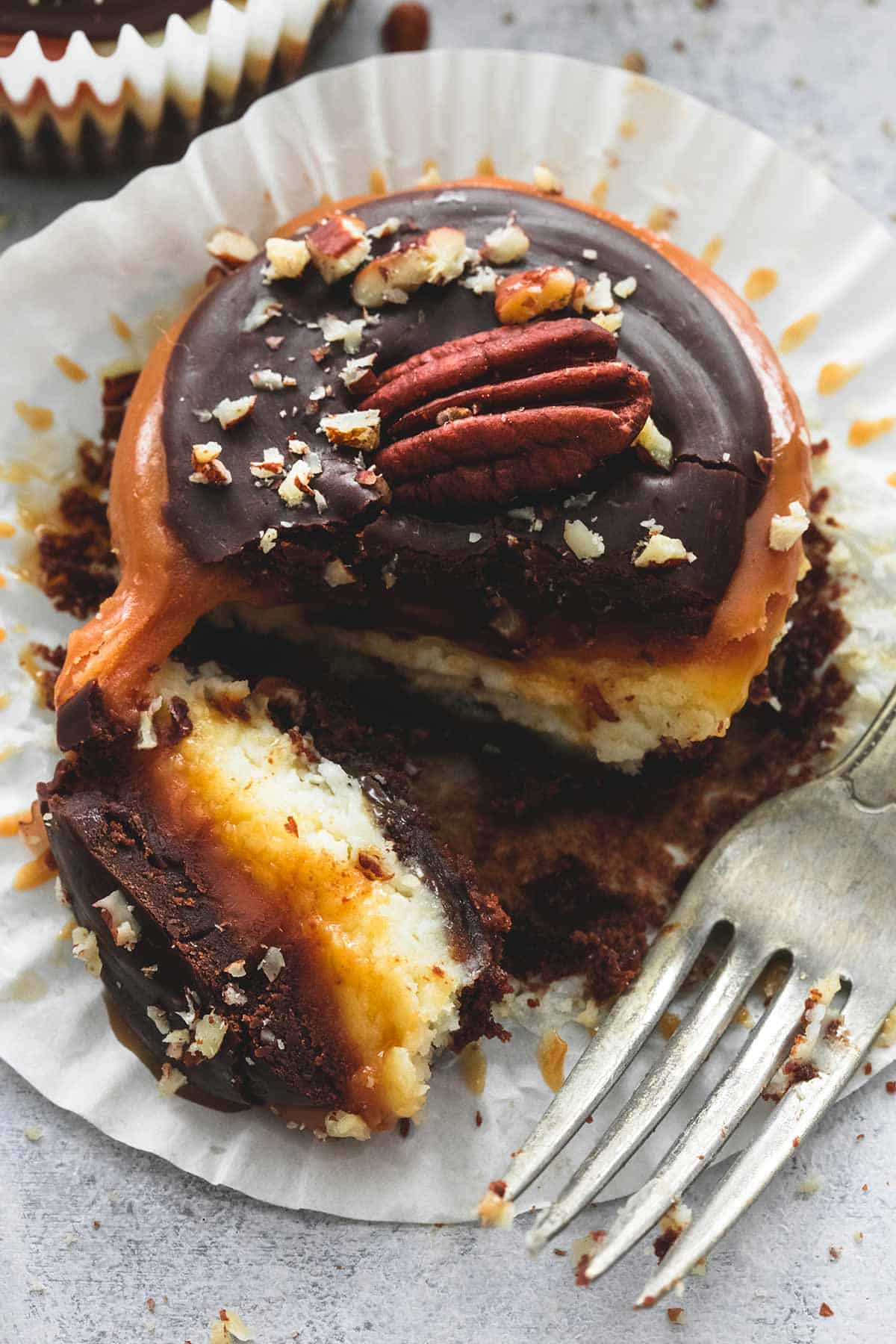 close up of a mini turtle cheesecakes with it's liner open and a bite separated from the rest of the cheesecake with a fork on the side.