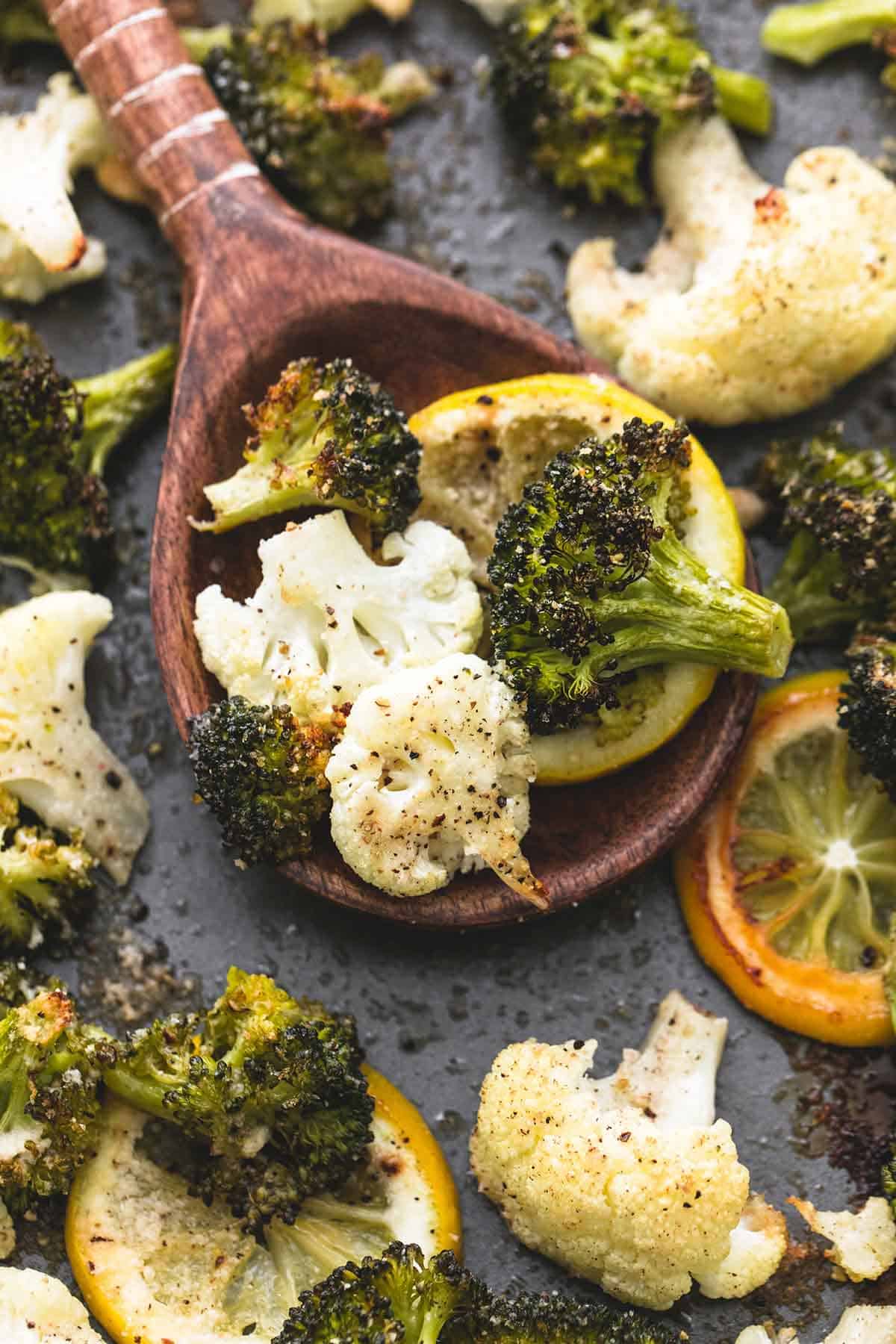 close up of roasted lemon garlic broccoli & cauliflower on a wooden serving spoon with more veggies around it.