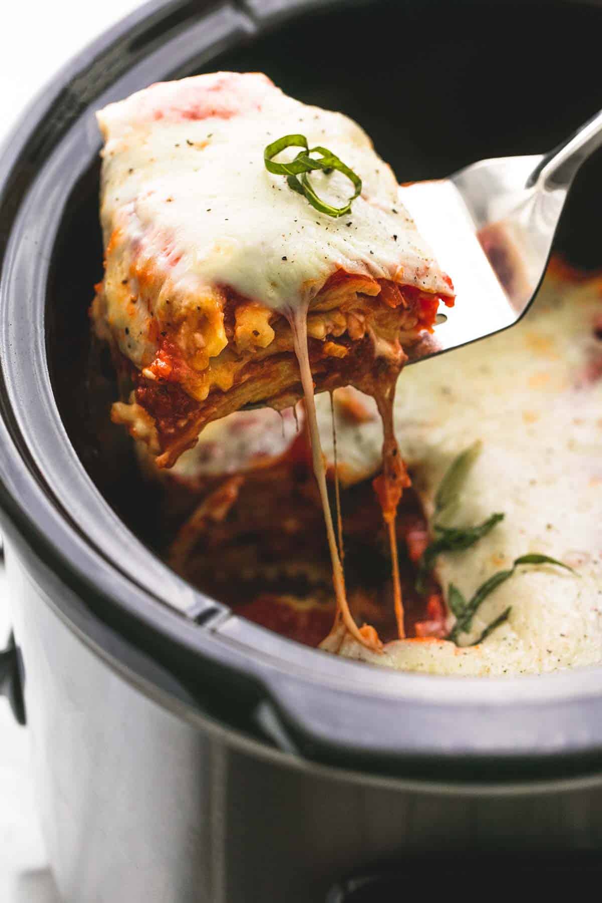 a spatula holding up some slow cooker ravioli lasagna from a slow cooker of more lasagna.
