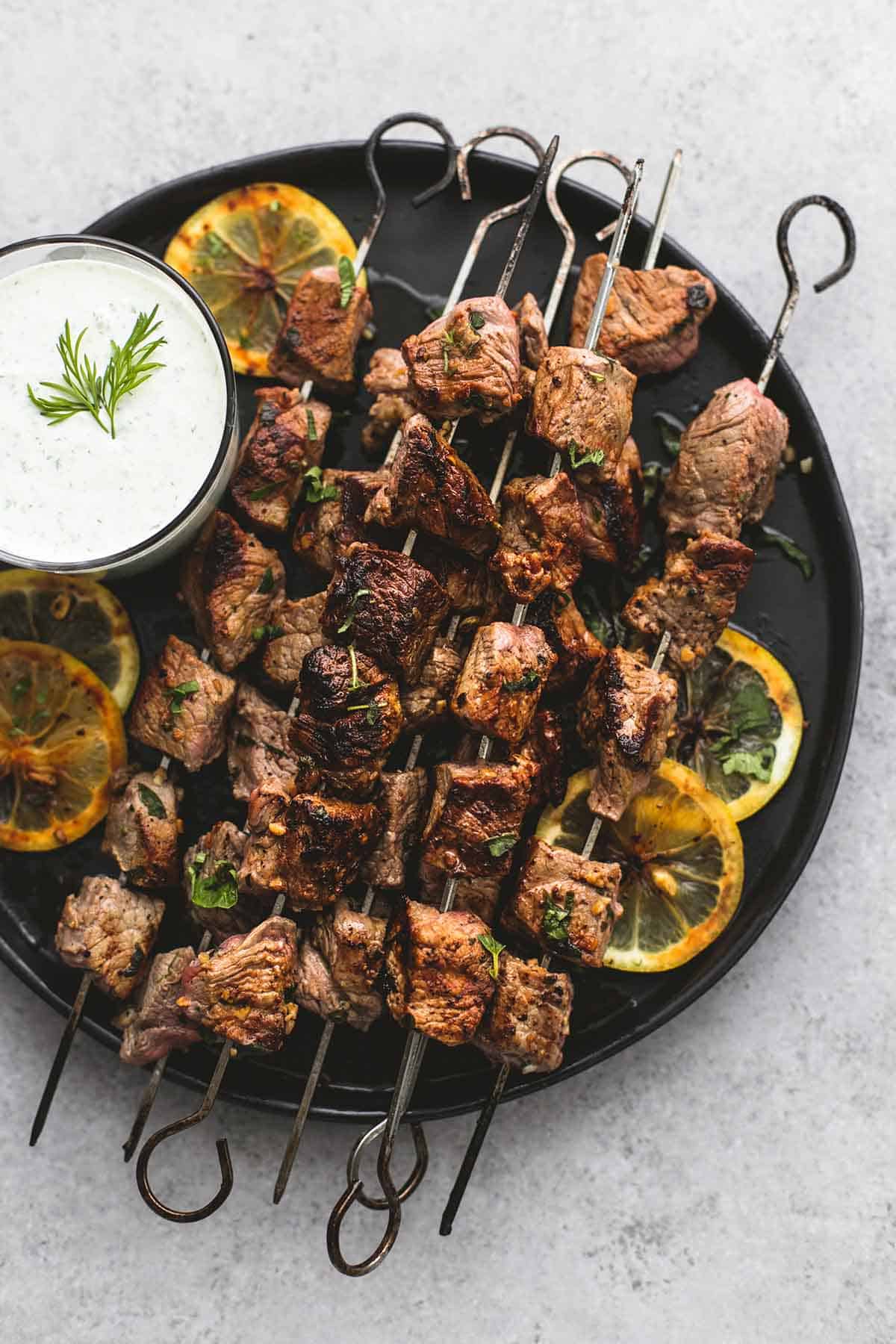top view of beef Souvlaki kebabs with tzatziki sauce on a plate.