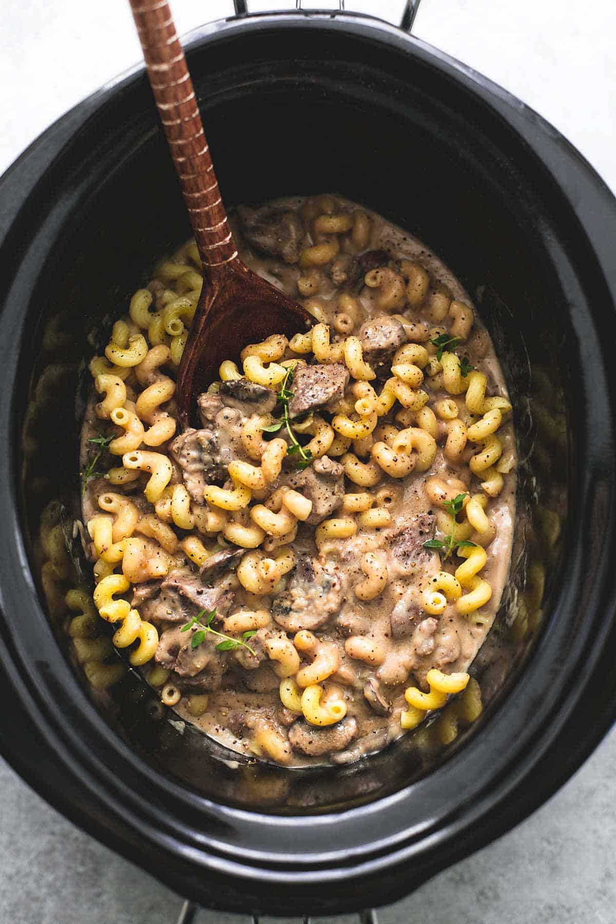 top view of slow cooker creamy beef stroganoff with a wooden serving spoon in a slow cooker.