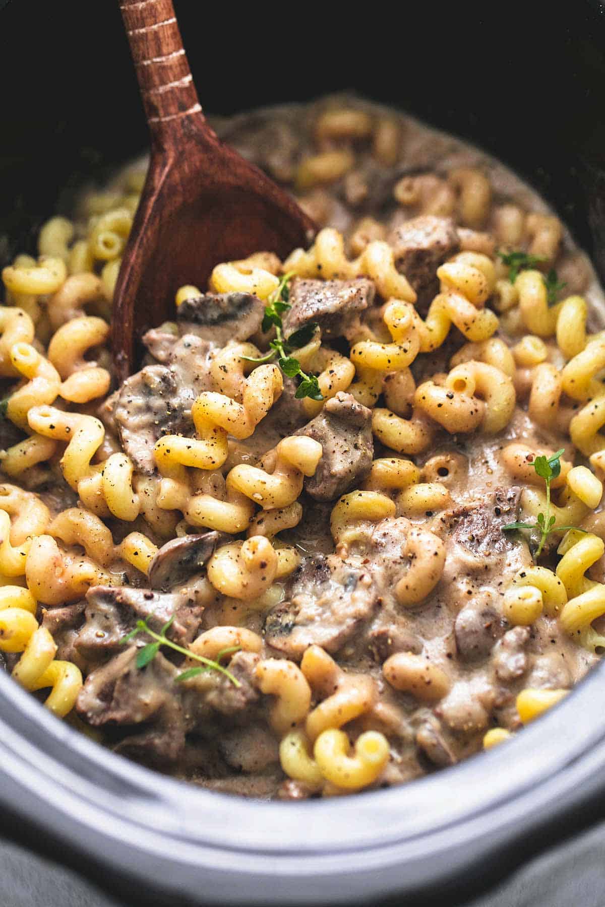 close up of slow cooker creamy beef stroganoff with a wooden serving spoon in a slow cooker.