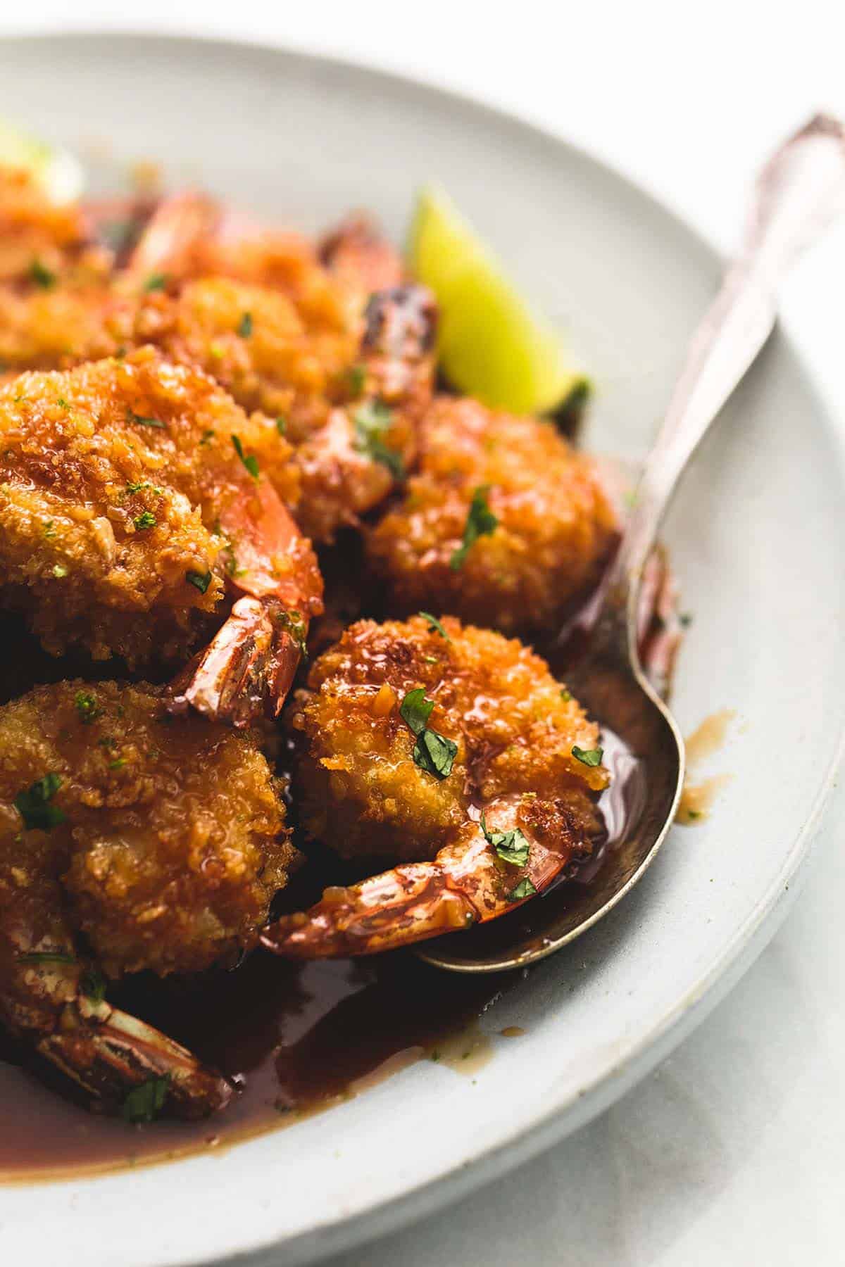 close up of baked crispy honey lime shrimp with a spoon on a plate.