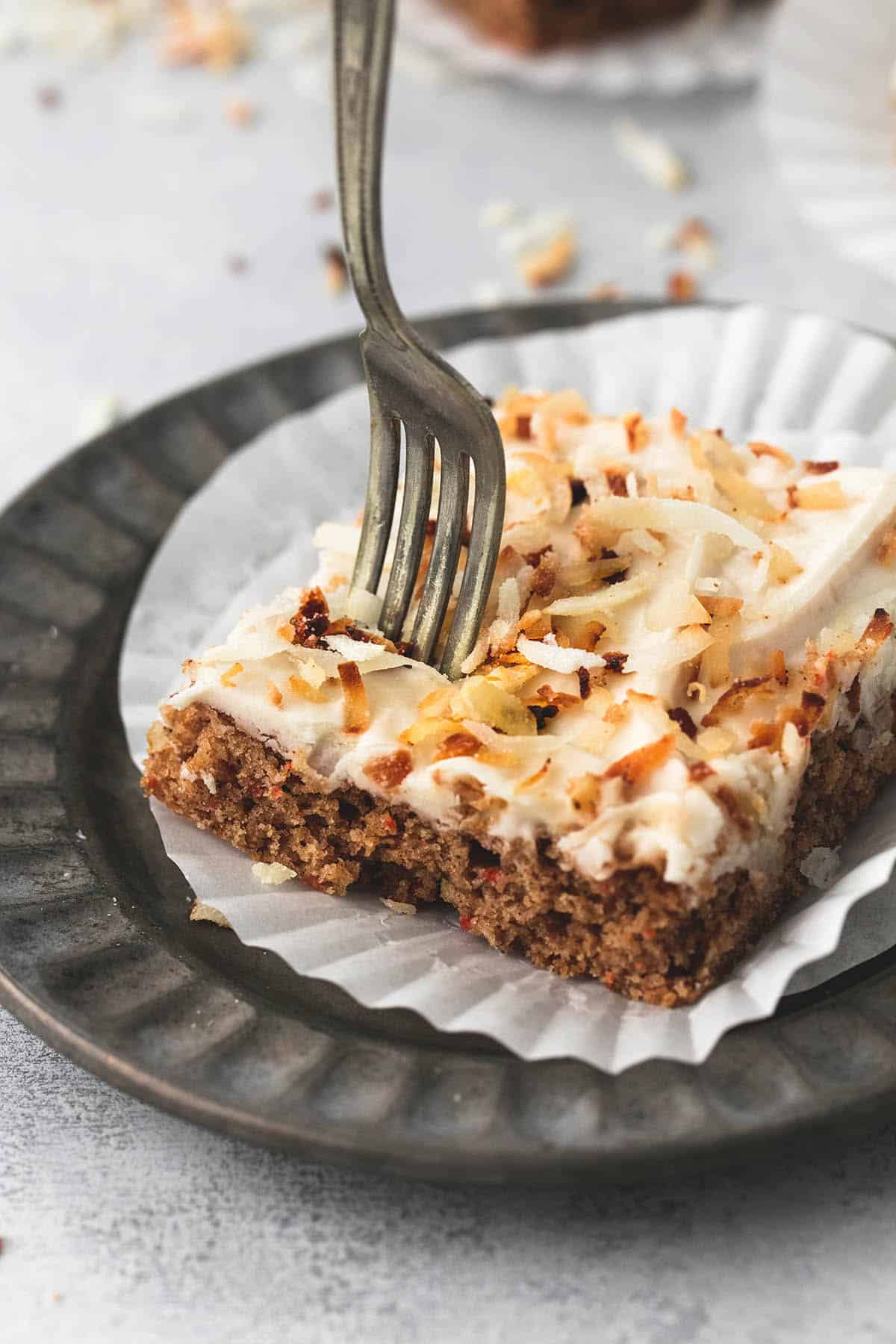 a carrot cake bars with coconut cream cheese frosting on a liner and on a plate with a fork in it.