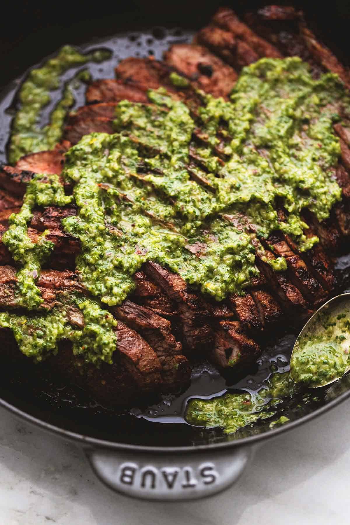 close up top view of flank steak with chimichurri sauce in a skillet.