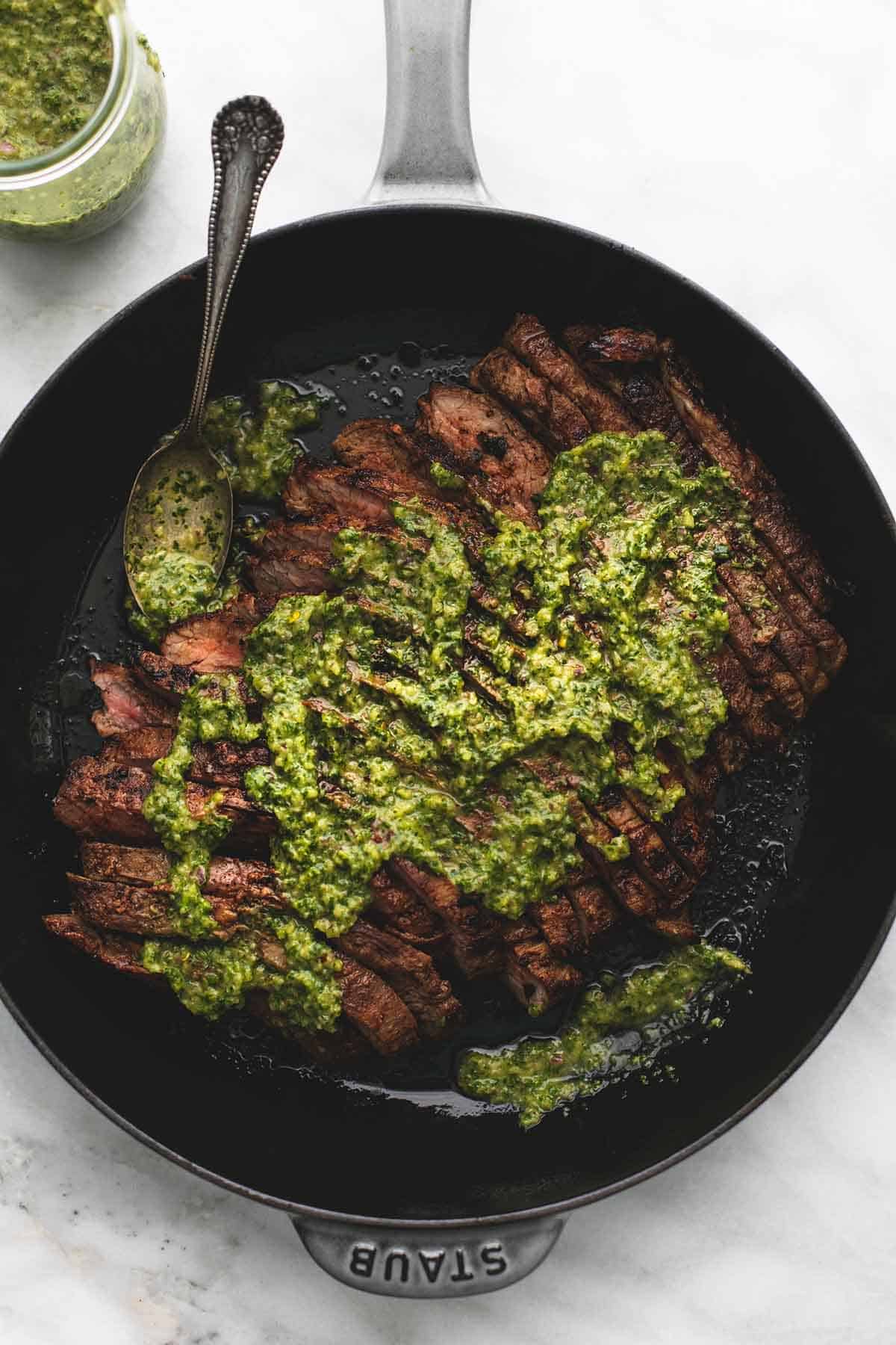 top view of flank steak with chimichurri sauce with a spoon in a skillet.