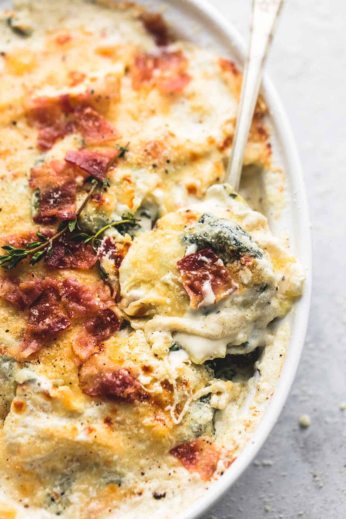 close up of ravioli alfredo bake with bacon and spinach with a spoon in a bowl.