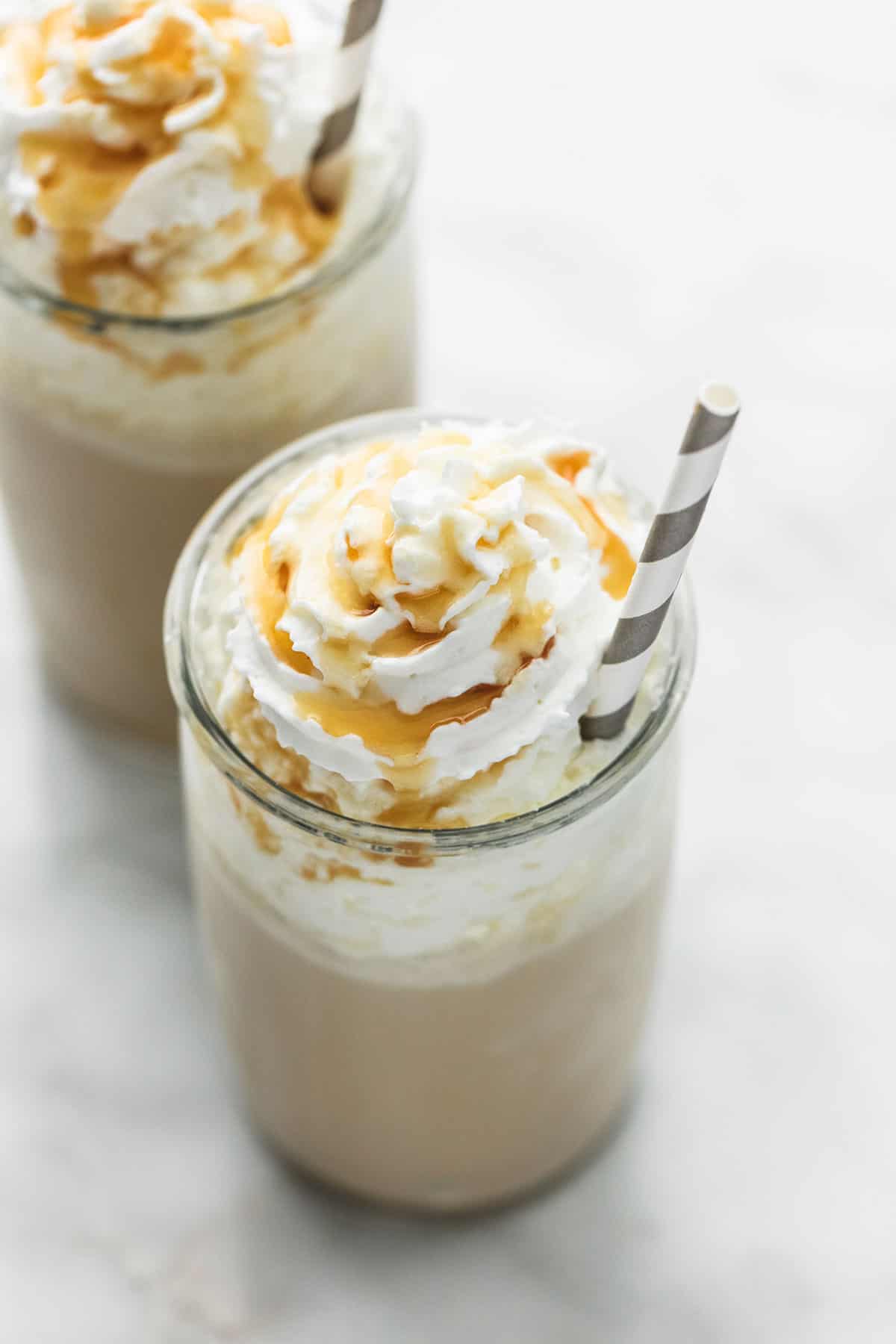 a salted caramel frappuccino (no coffee) in a glass with a straw with another frappuccino in the background.