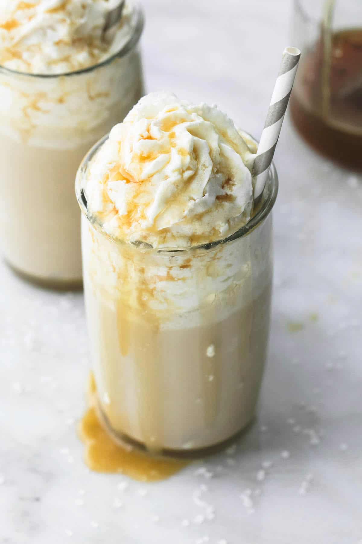 salted caramel frappuccino (no coffee) in a glass with a straw with another frappuccino in a glass in the background.