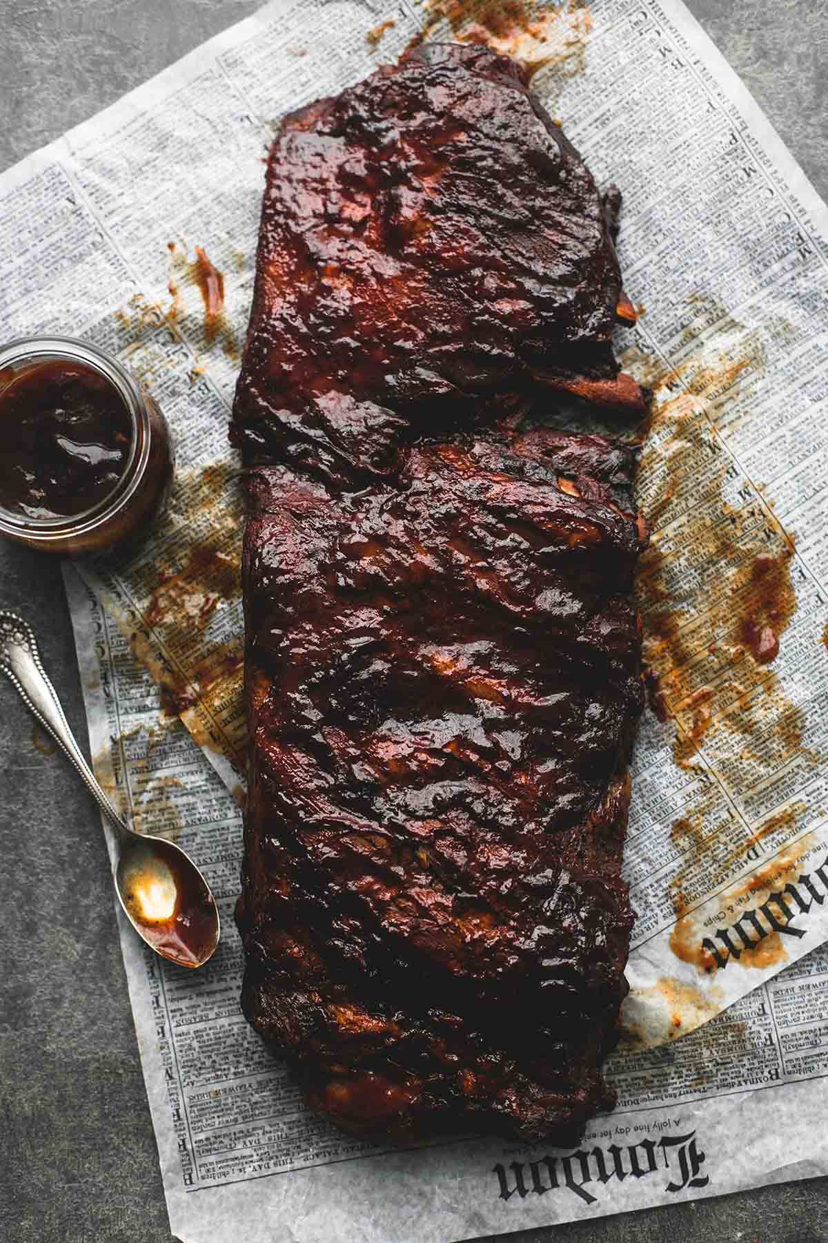 top view of slow cooker bbq ribs on newspaper with a spoon and jar of sauce on the side.