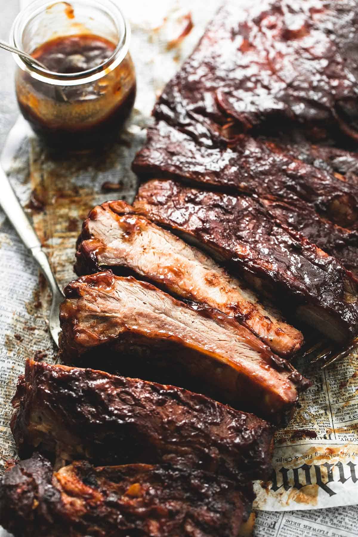 close up of slow cooker bbq ribs with a fork and a jar of sauce on the side.