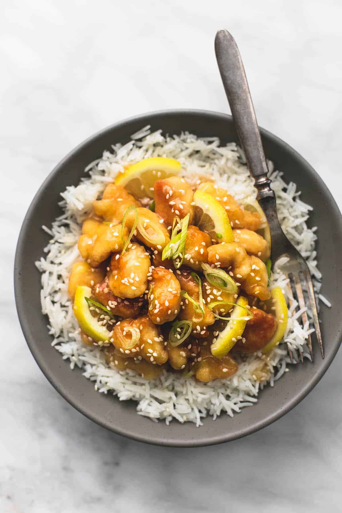 top view of sticky Chinese lemon chicken on rice with a fork on a plate.