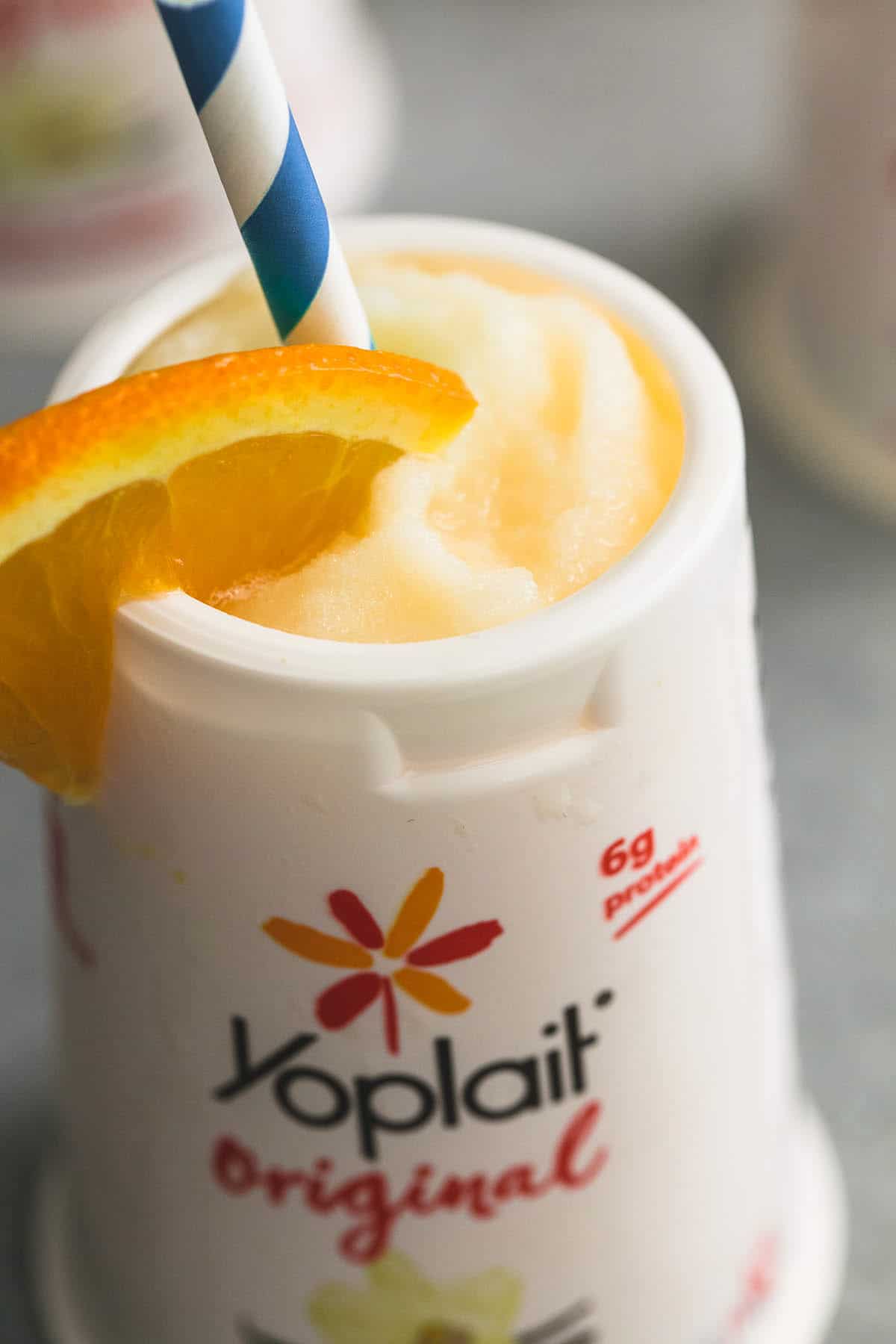 orange julius in a Yoplait container with a orange slice and straw.