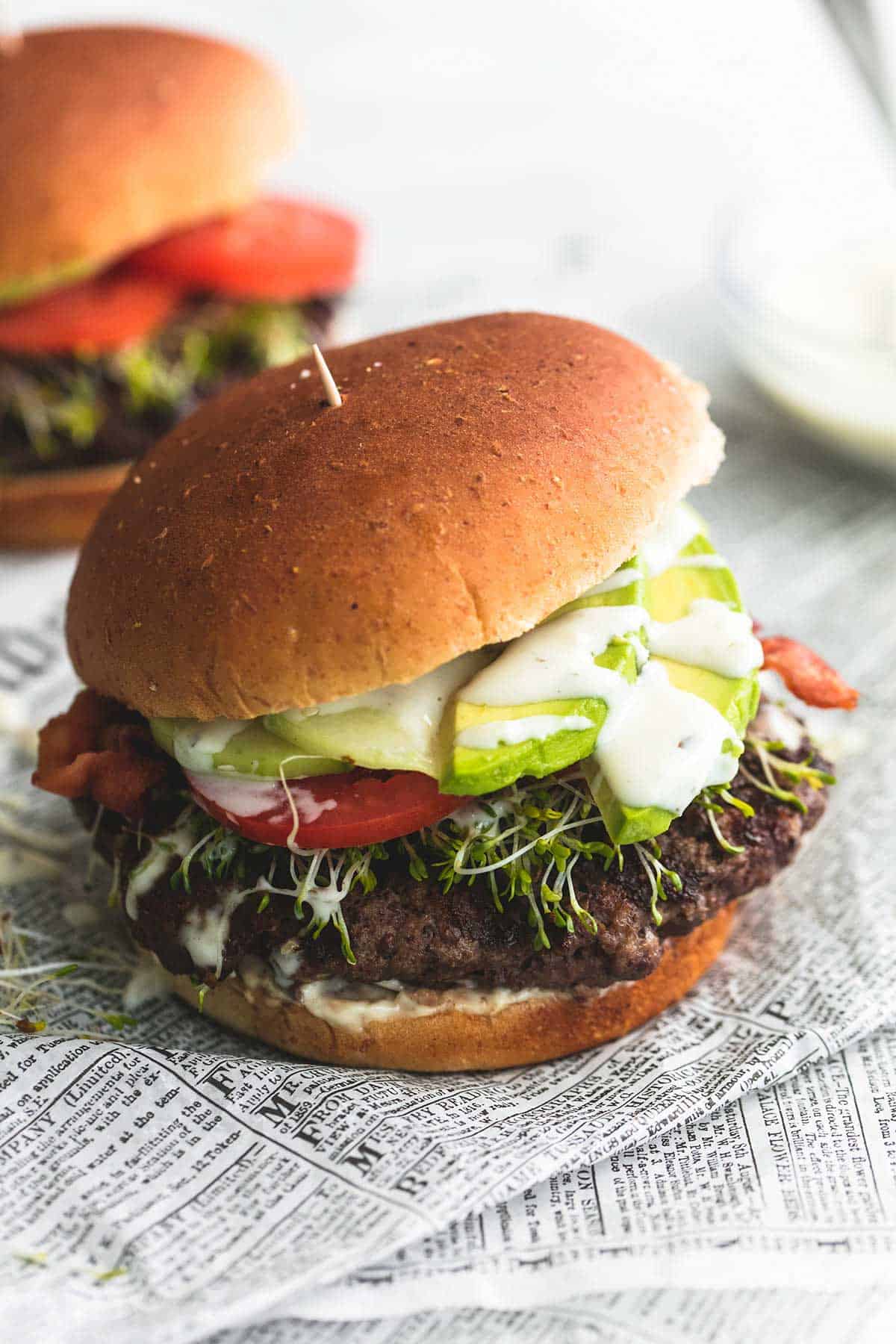 a California club burger with another burger and a bowl of ranch dressing faded in the background.