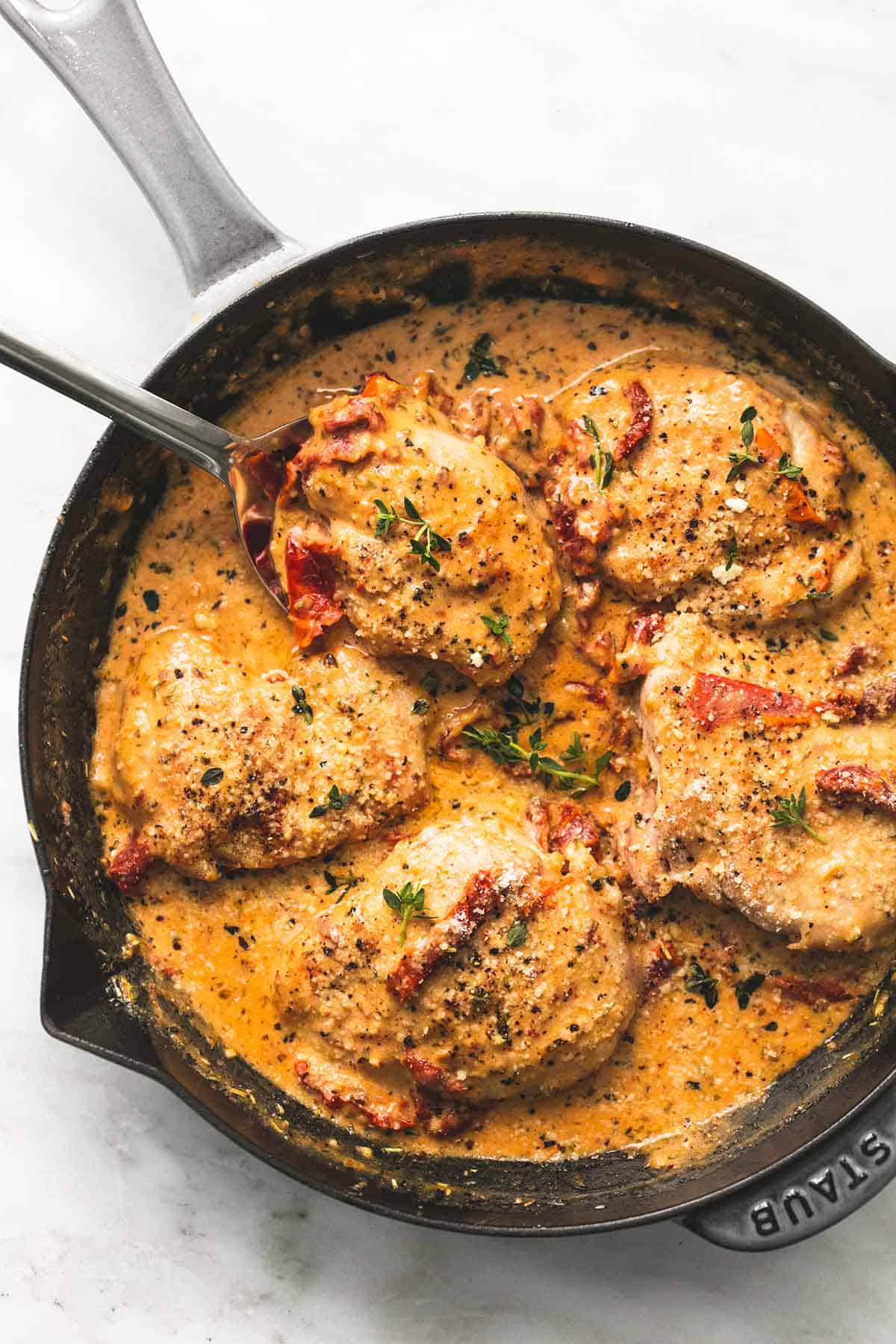 top view of chicken in sun dried tomato cream sauce with a spoon in a skillet.