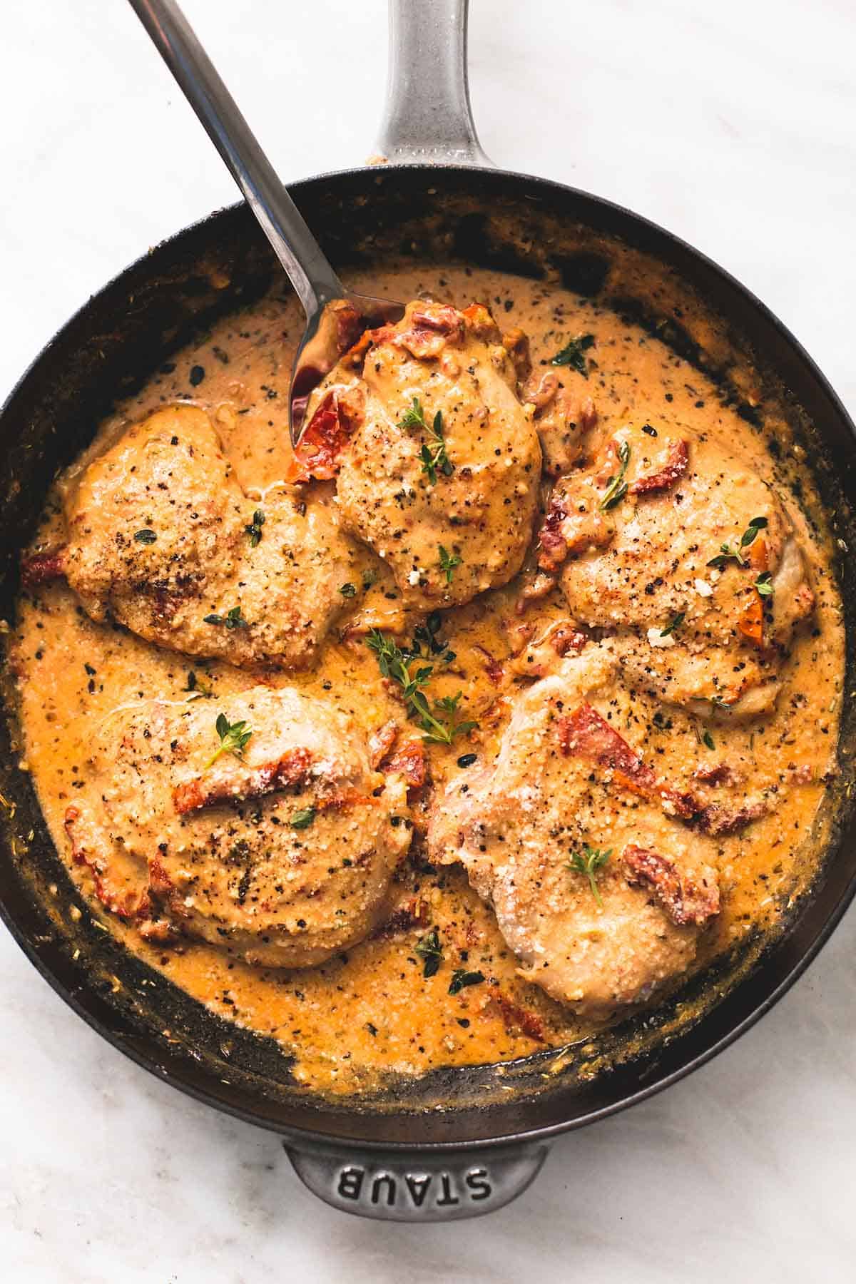 top view of chicken in sun dried tomato cream sauce with a spoon in a skillet.