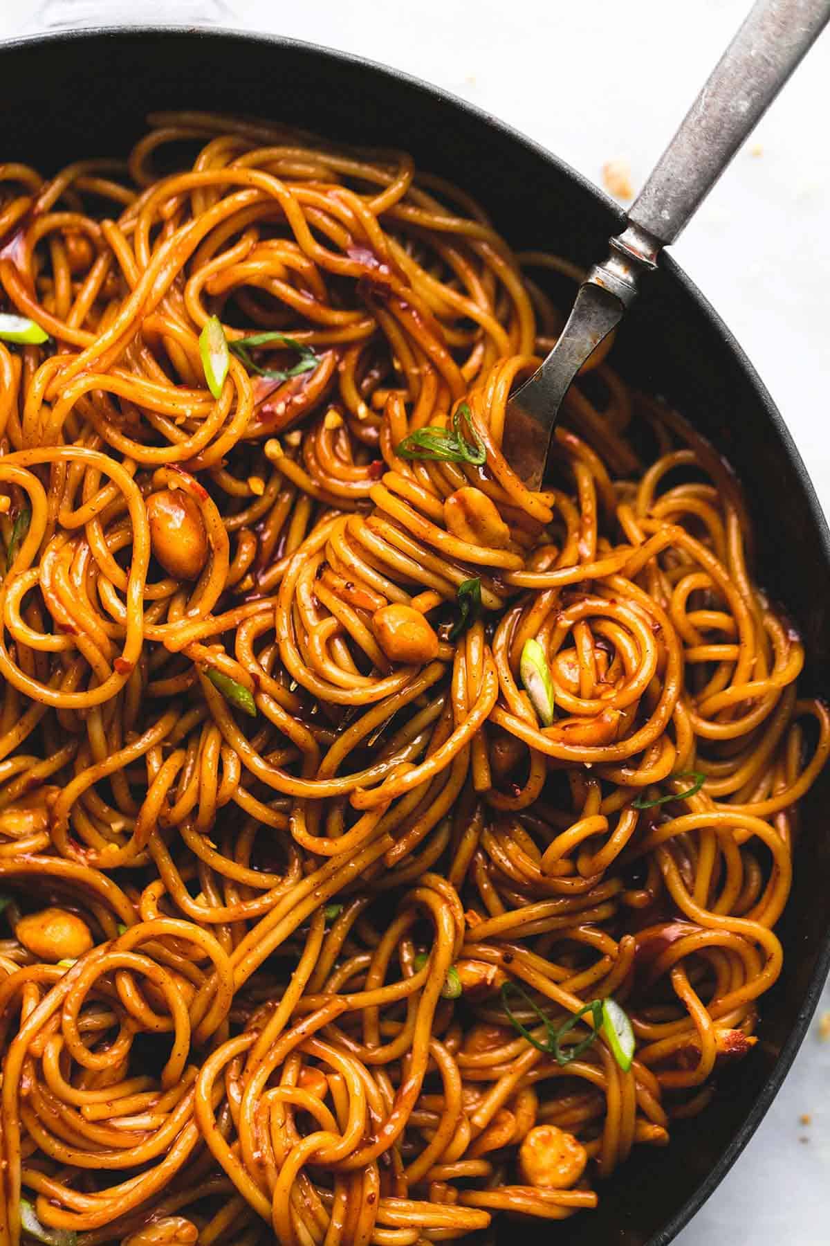close up of kung pao noodles with a fork in a pan.