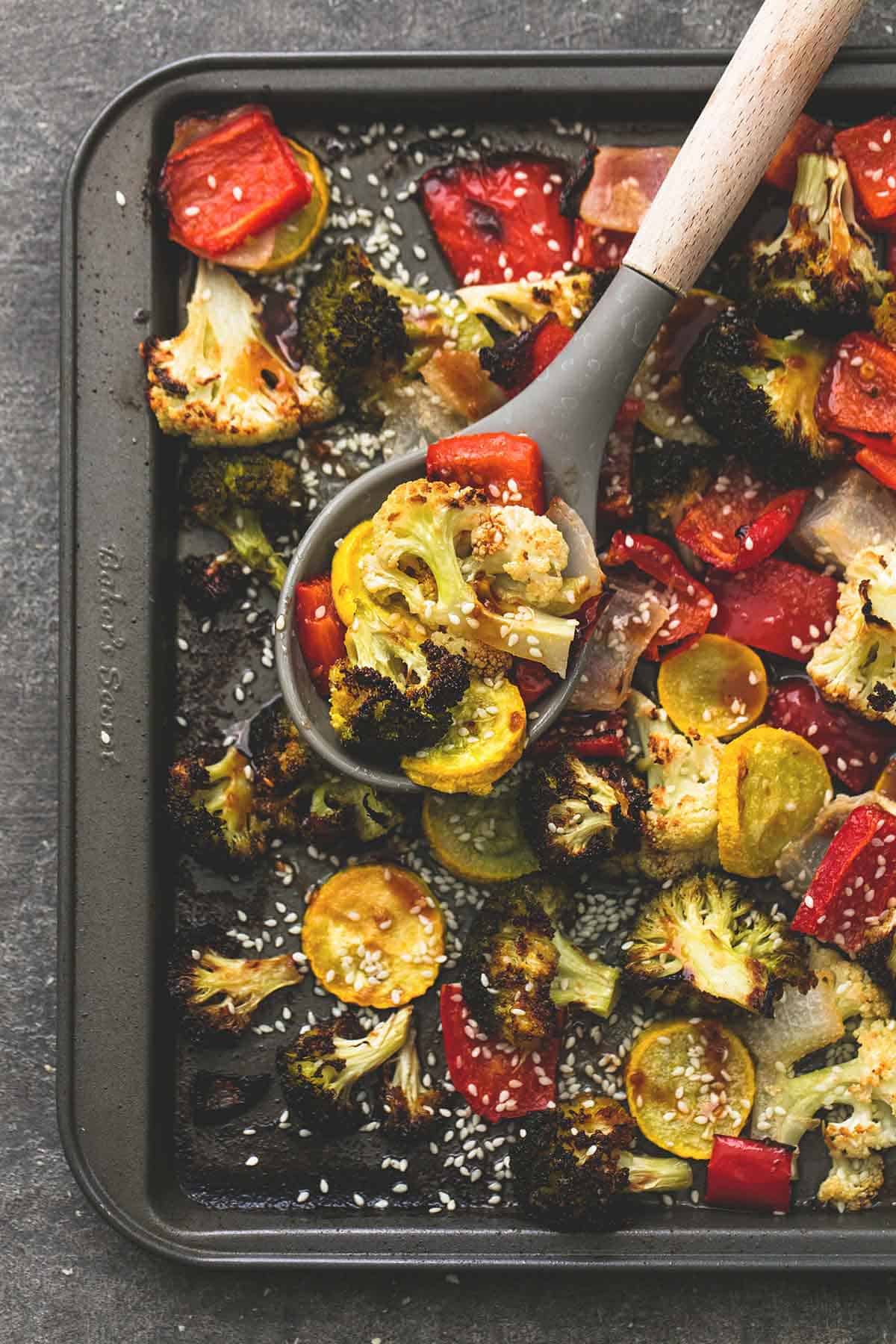 top view of roasted Asian vegetable medley with a serving spoon on a baking sheet.