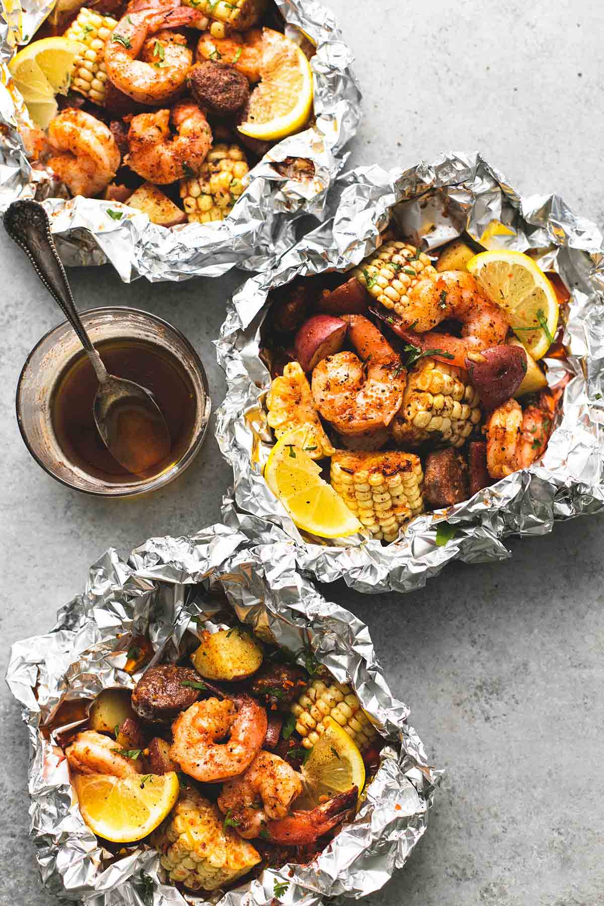top view of shrimp boil foil packs with brown butter sauce in a glass with a spoon.