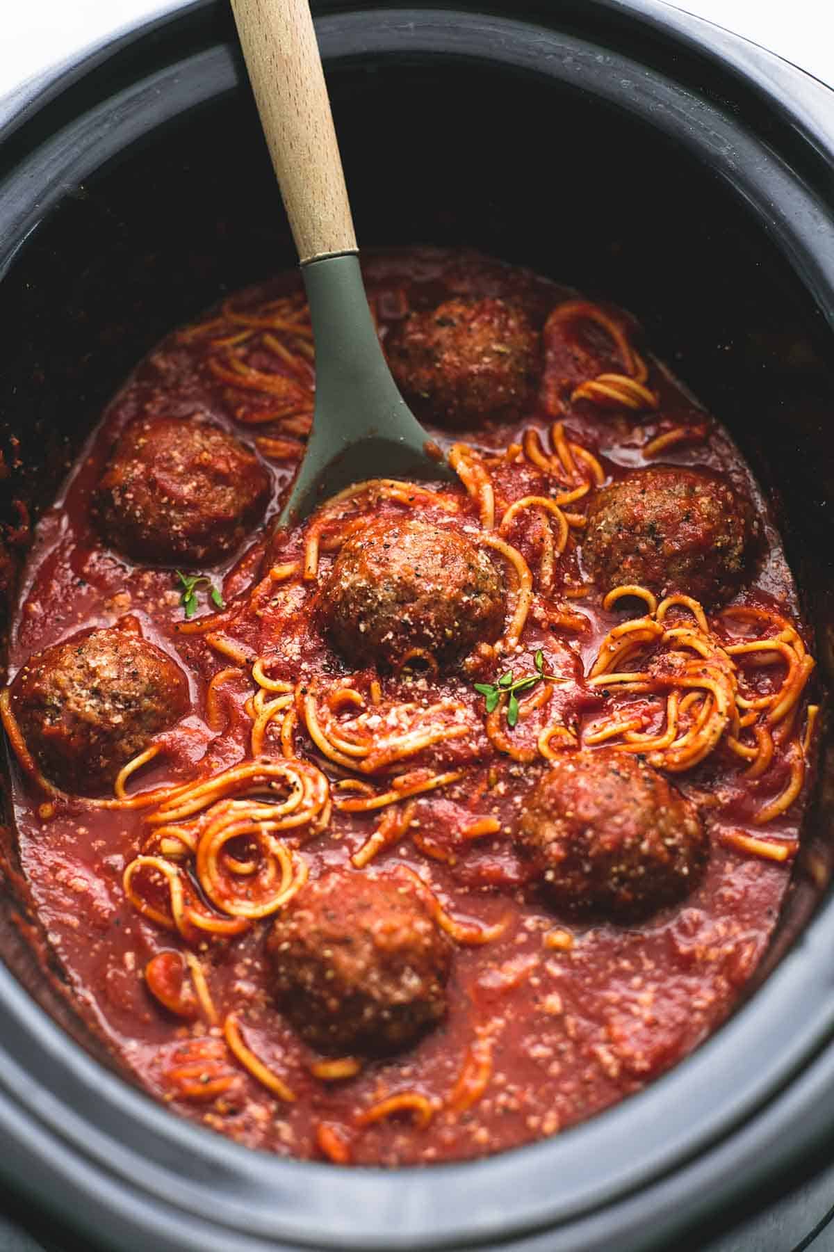 top view of slow cooker spaghetti and meatballs with a serving spoon in a slow cooker.