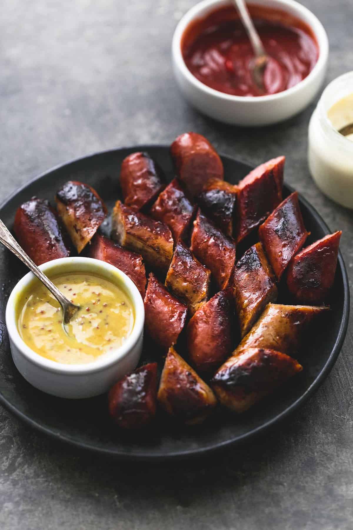 grilled sausages with a bowl of dipping sauce on a plate with more dipping sauce on the side.