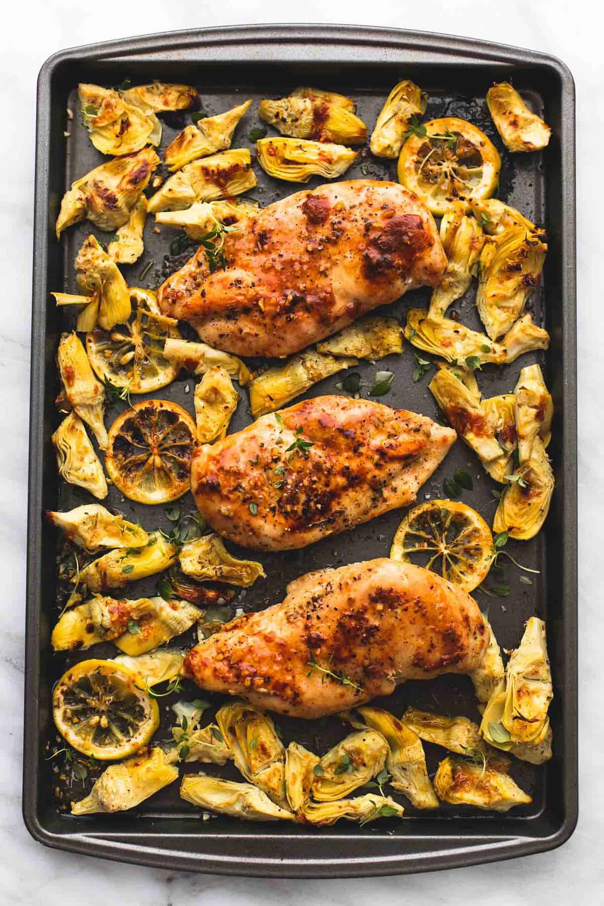 top view of baked lemon chicken and artichokes in a baking sheet.