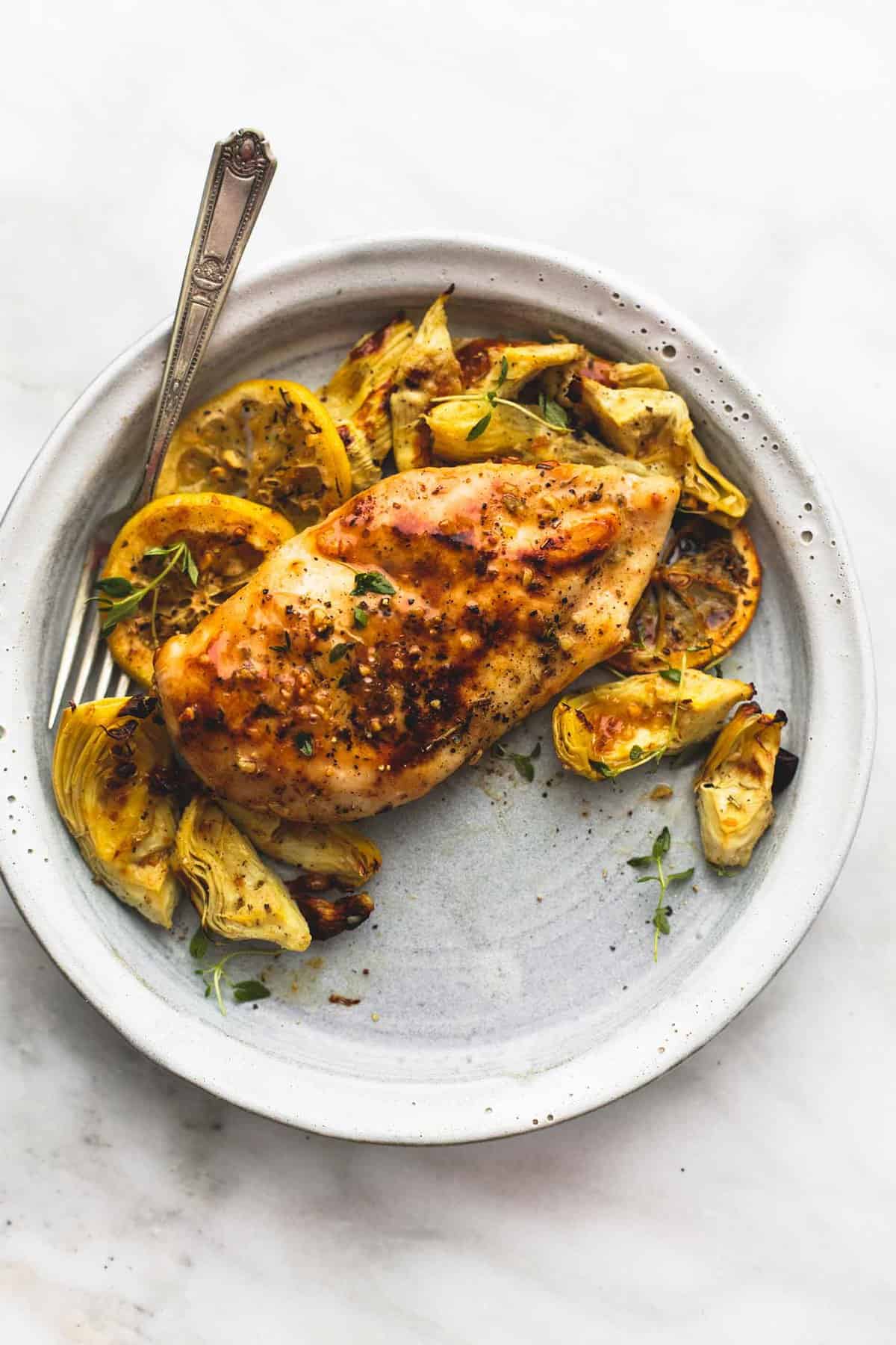 top view of baked lemon chicken and artichokes and a fork on a plate.