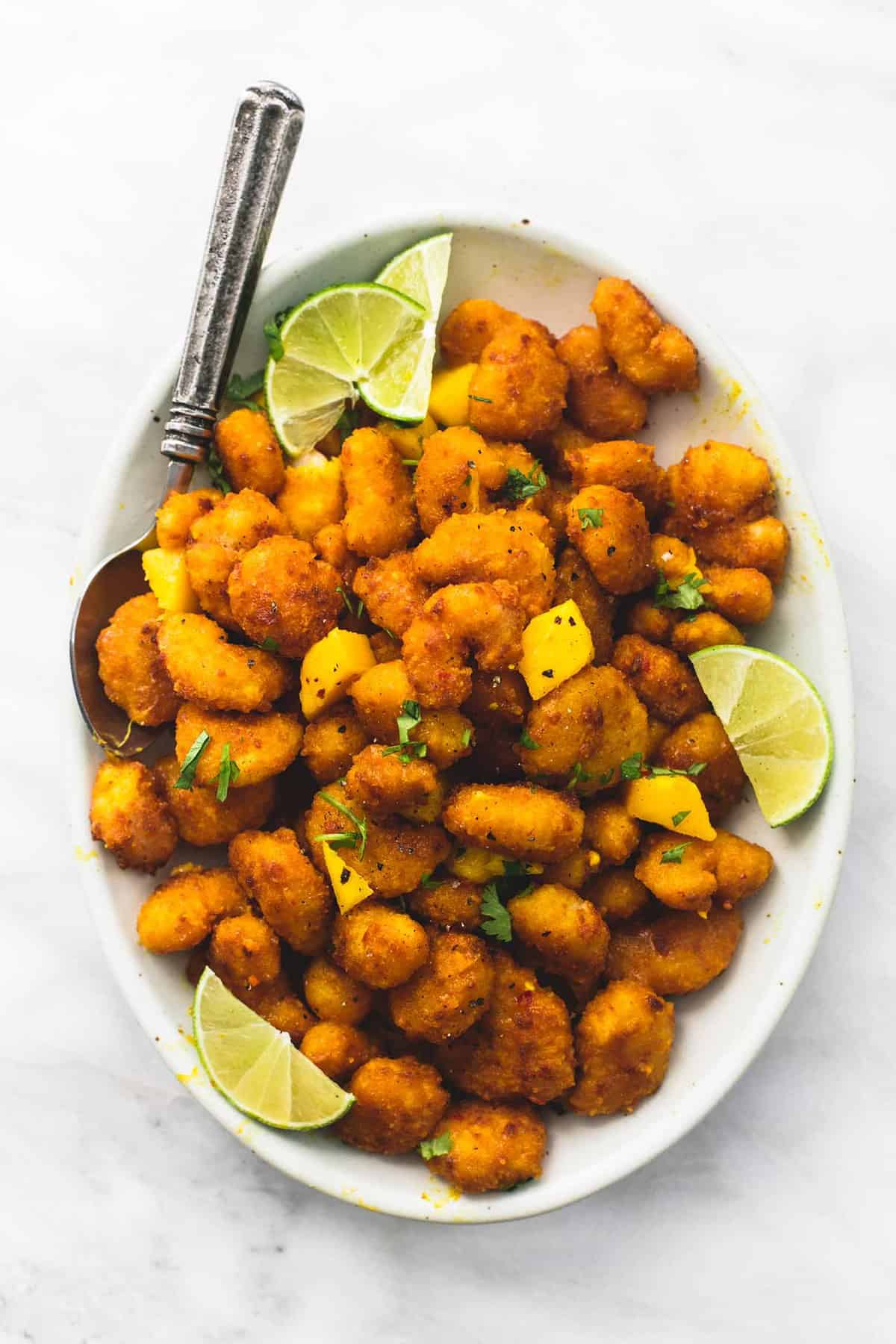 top view of mango habanero popcorn shrimp with lime slices and a spoon on a plate.