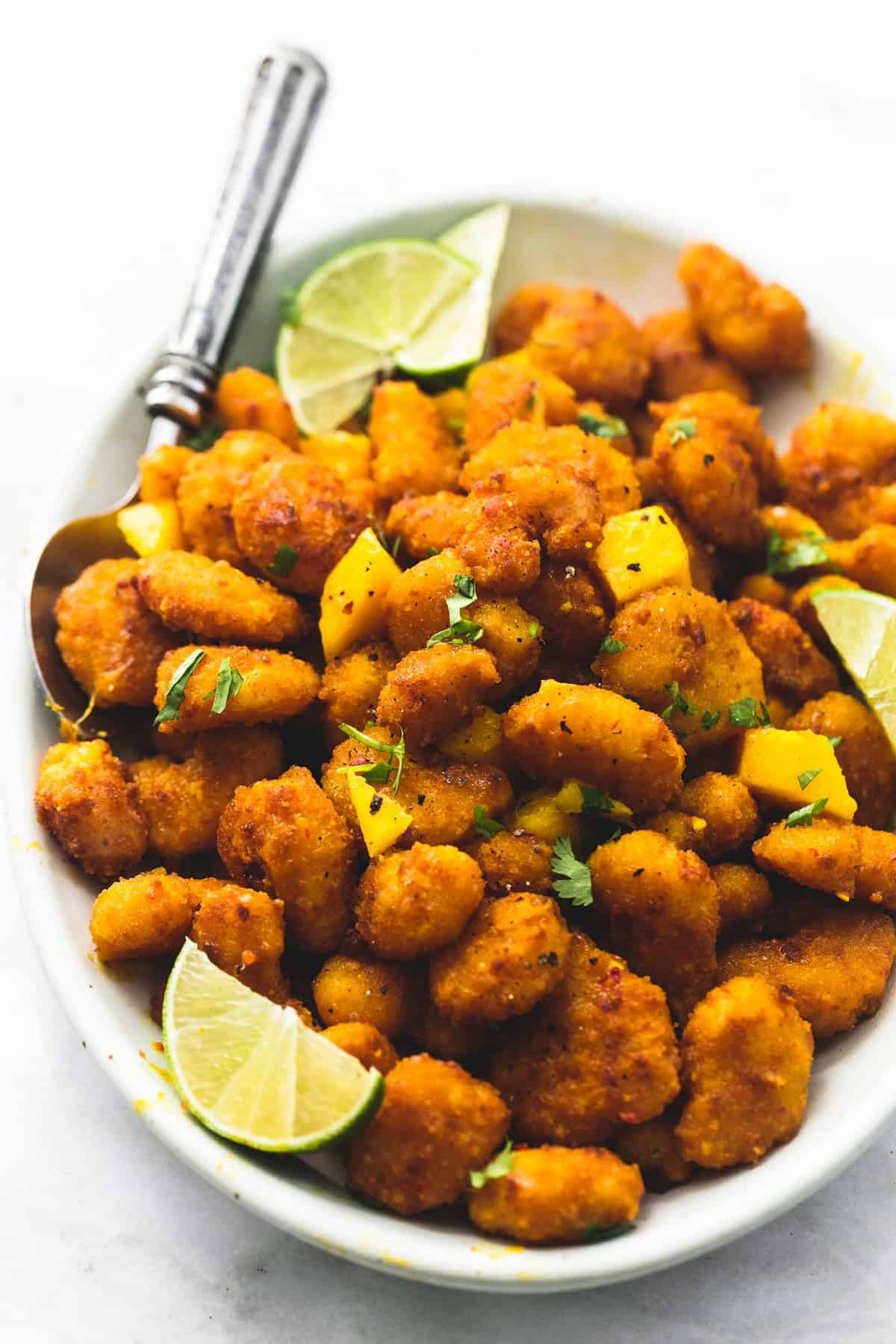 mango habanero popcorn shrimp with lime slices and a spoon on a plate.