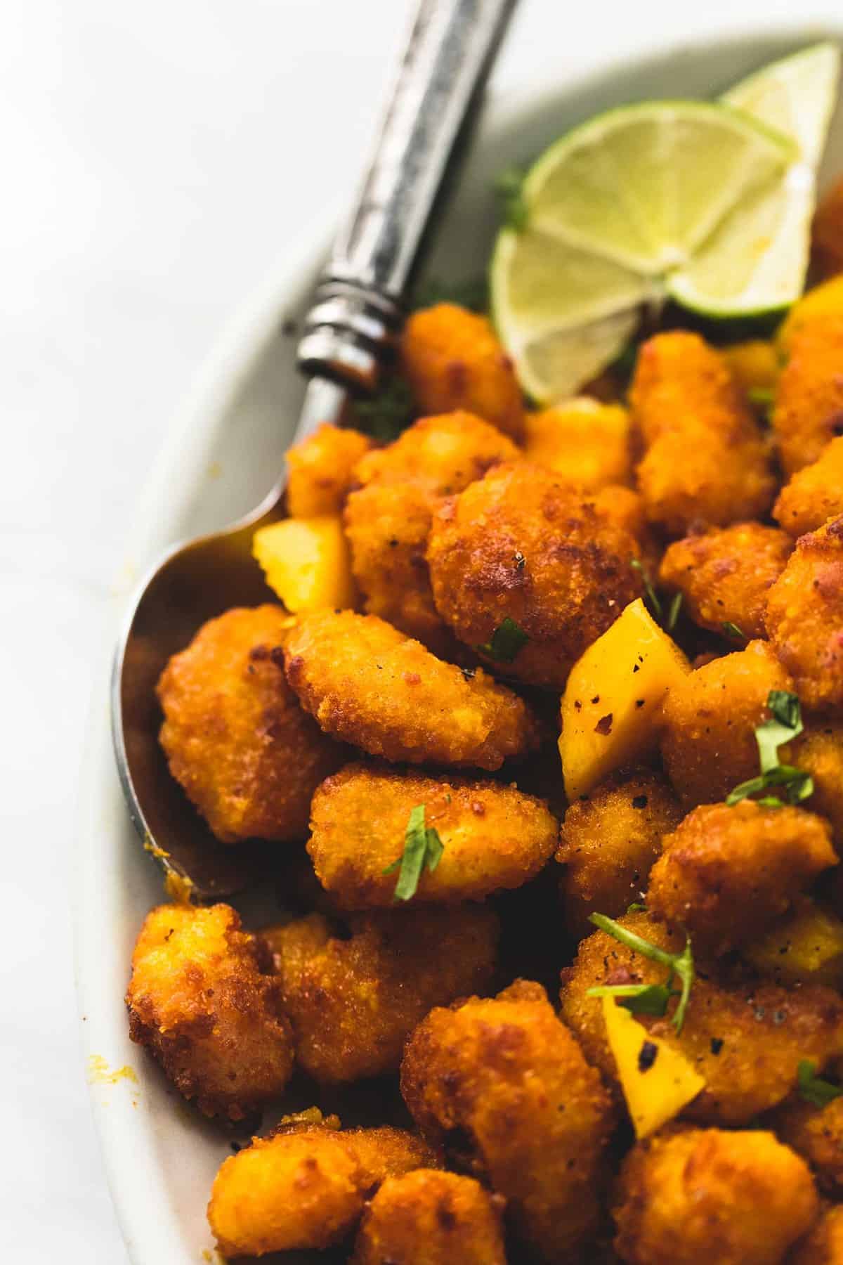 close up of mango habanero popcorn shrimp with lime slices and a spoon on a plate.