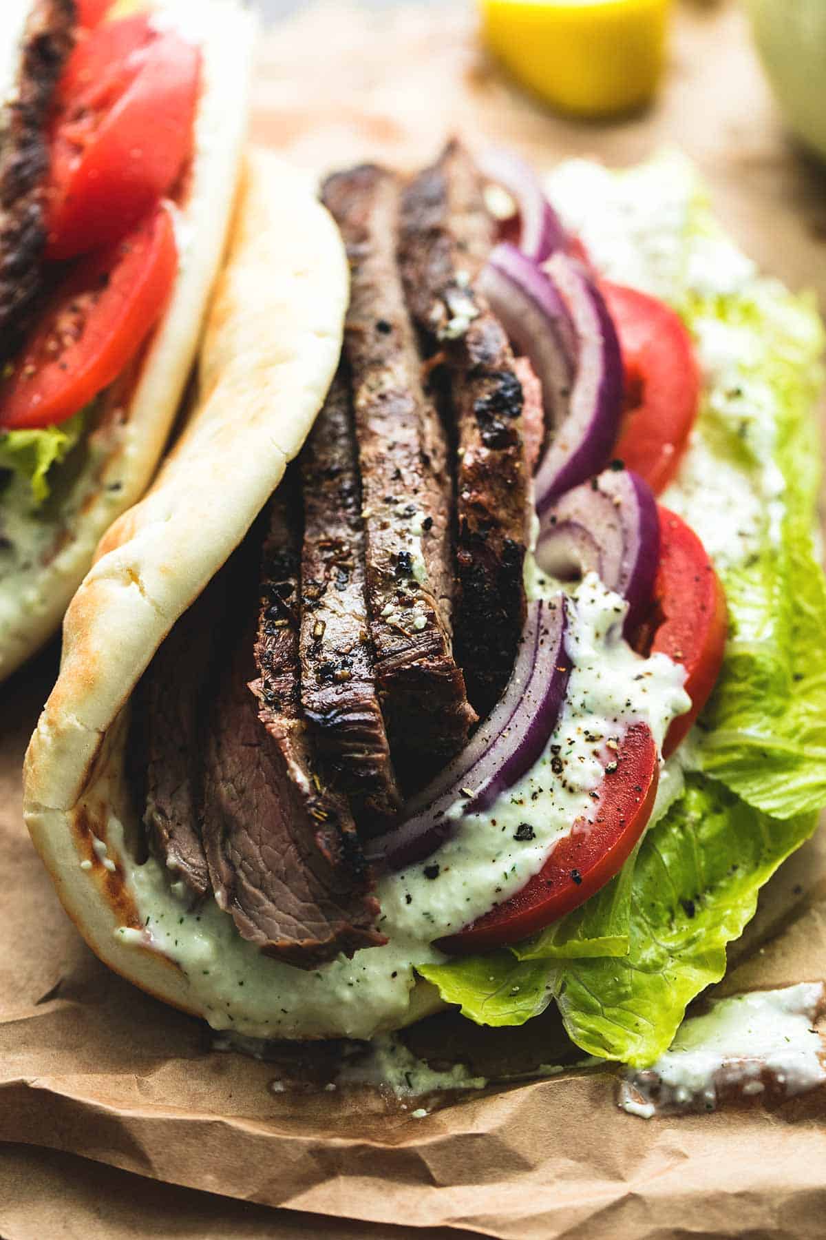 close up of a steak gyros with tzatziki cucumber sauce with another gyros. on the side.