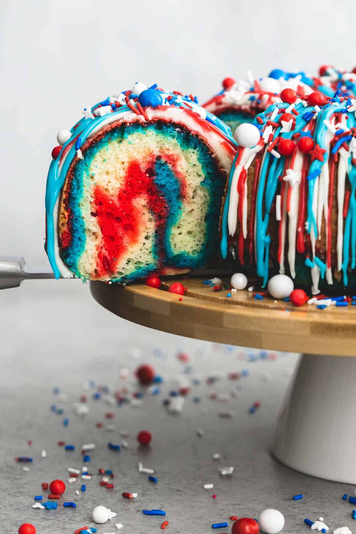 firecracker bundt cake frosted with red, white, and blue frosting and topped with a spatula grabbing a slice.