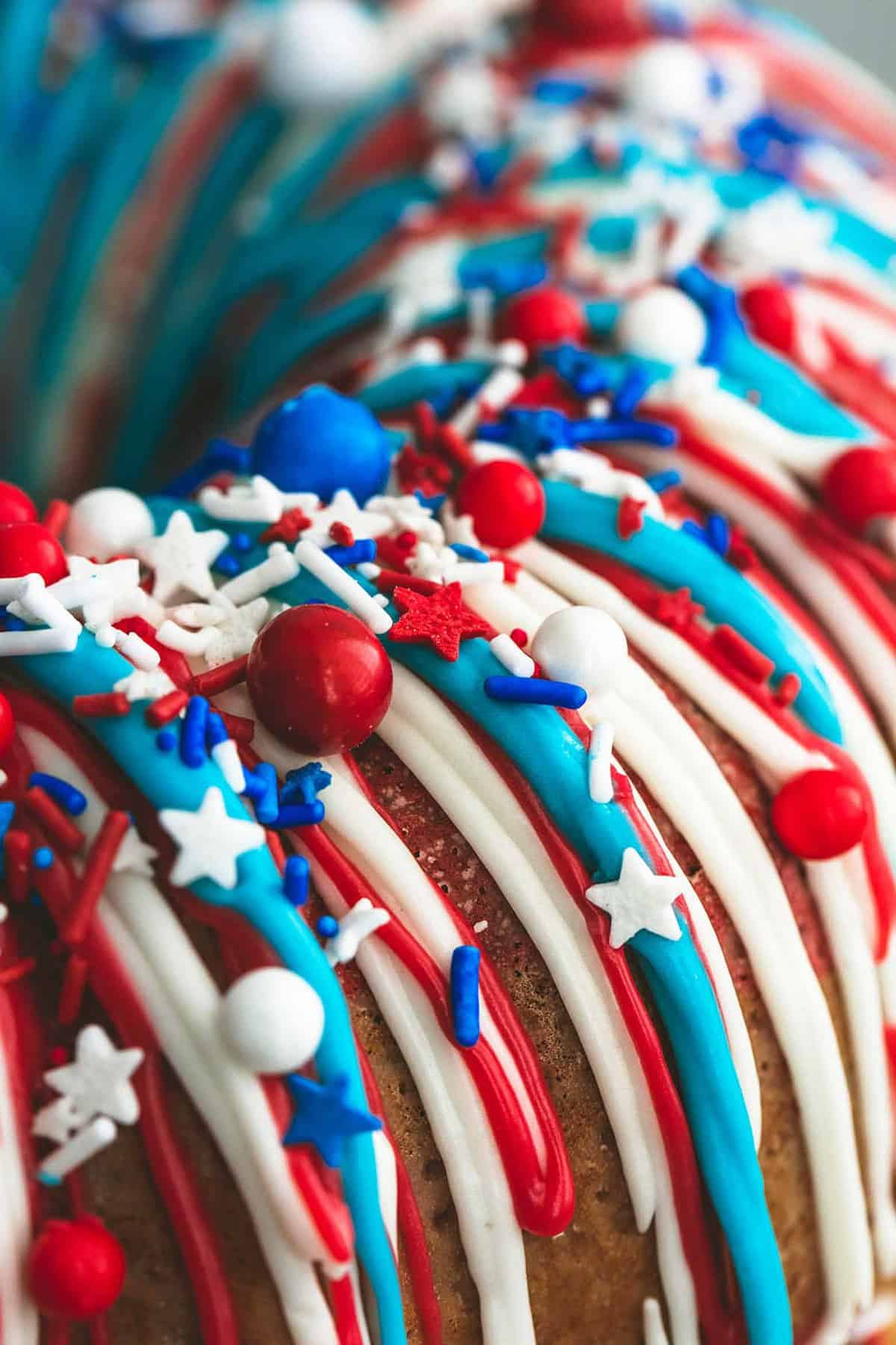 close up of firecracker bundt cake frosted with red, white, and blue frosting and topped with sprinkles.